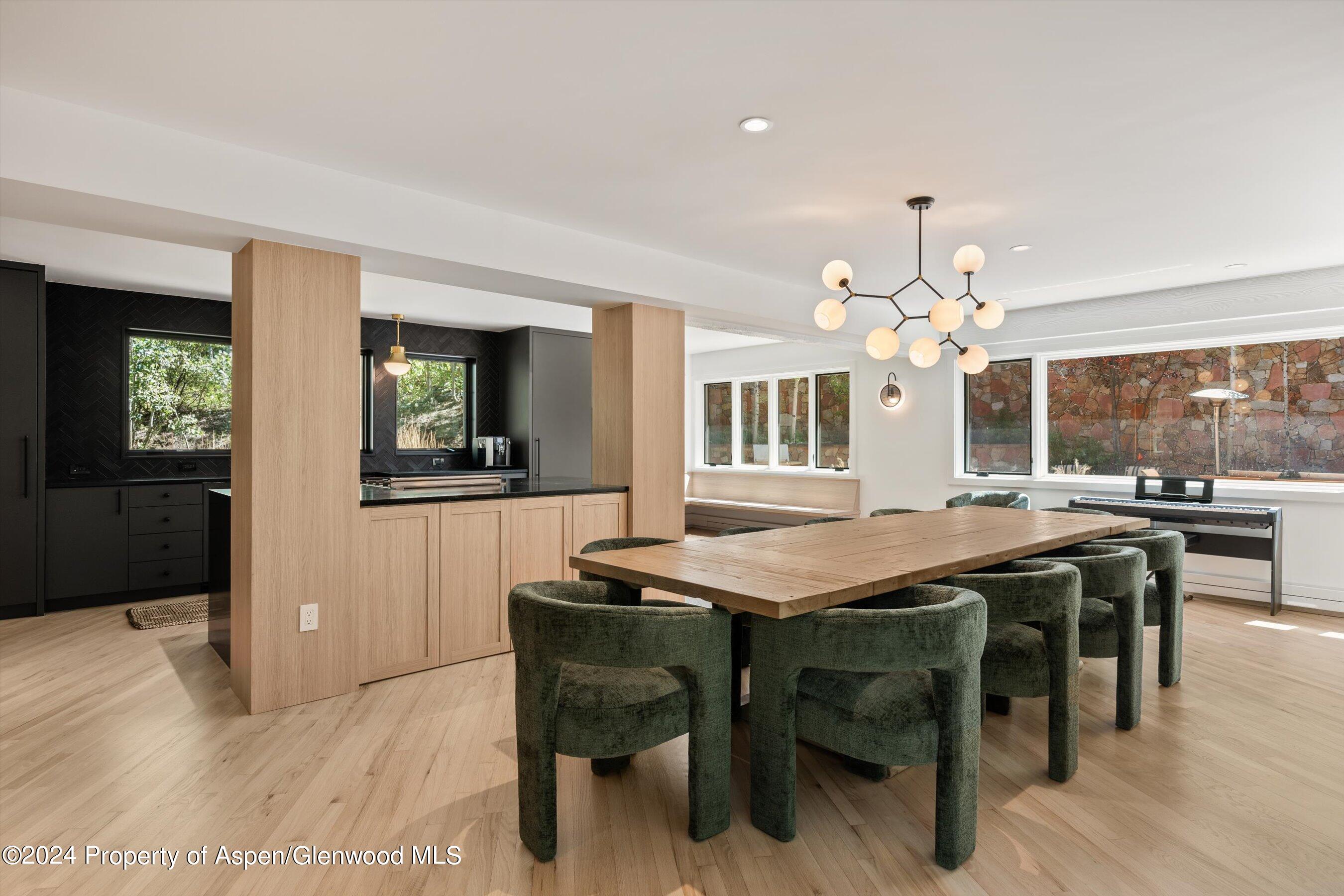 Dining area with a long wood table, green upholstered chairs, and an adjoining black kitchen.