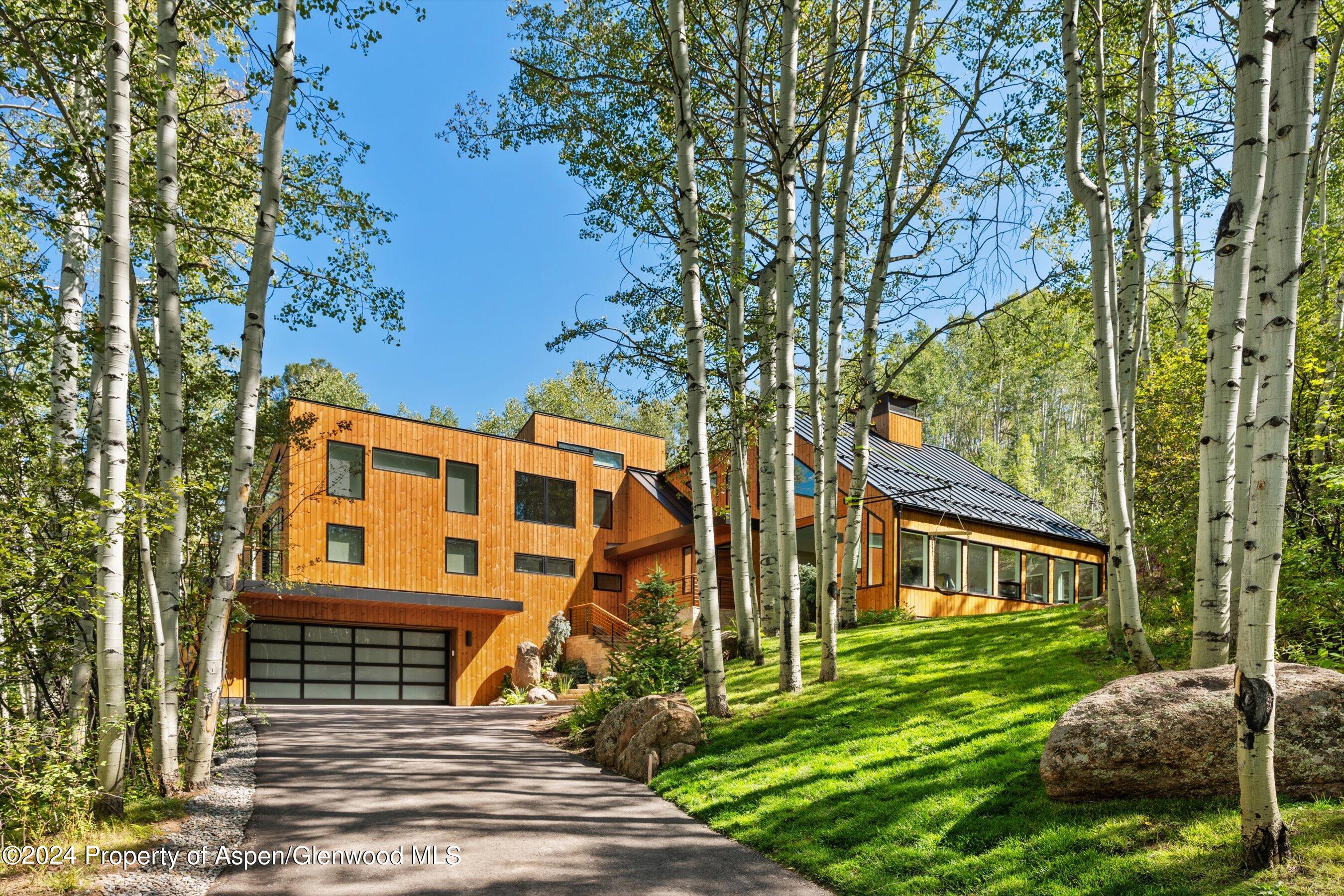 Modern wood-sided home among aspen trees, with a metal roof, driveway, and attached garage.