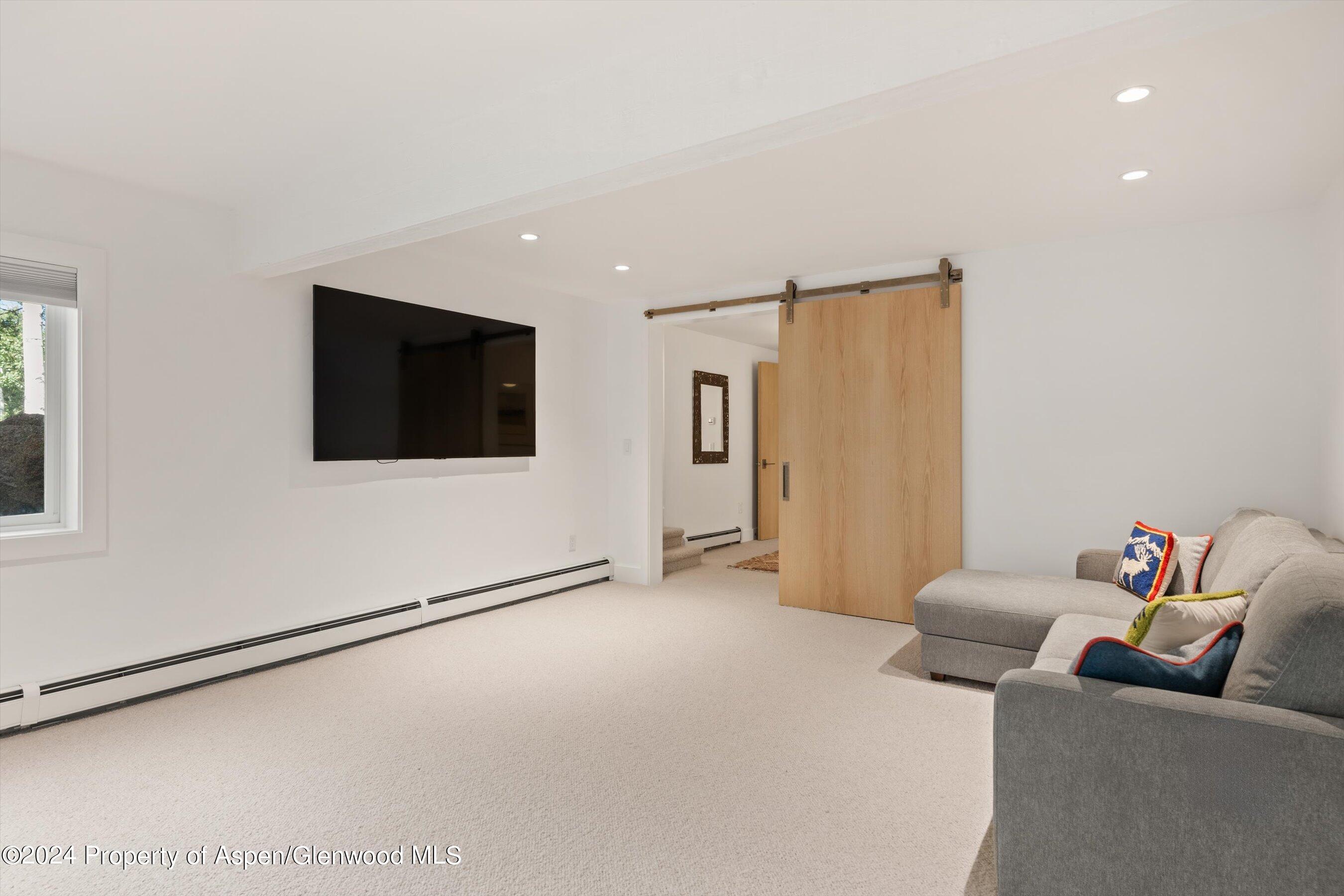 Furnished media room with a wall-mounted television, gray sectional, and sliding wood barn door.