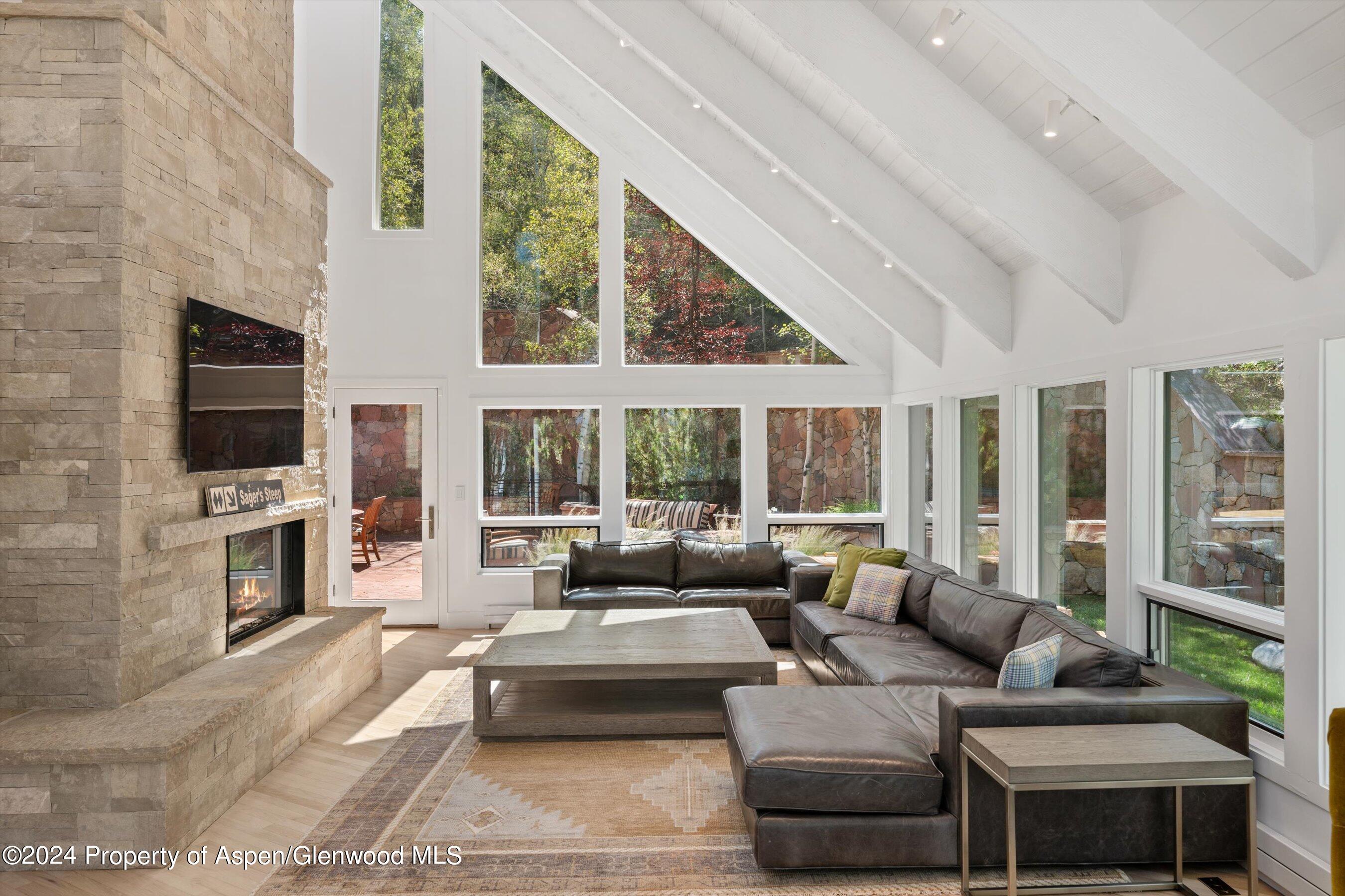 Furnished living room with a soaring vaulted ceiling, stone fireplace, and large windows.