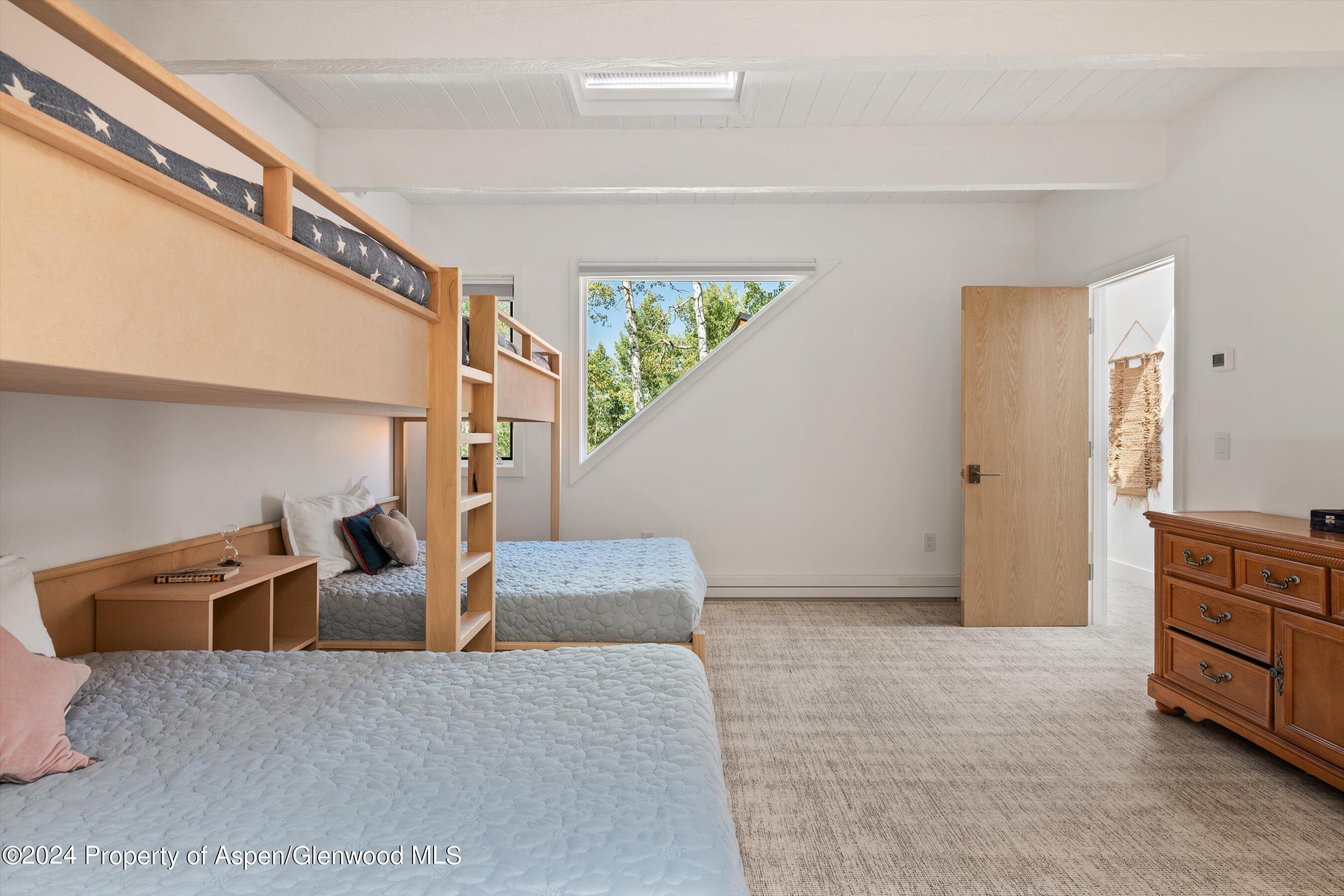 Bedroom with wooden bunk beds, blue bedding, and an angled window overlooking trees.