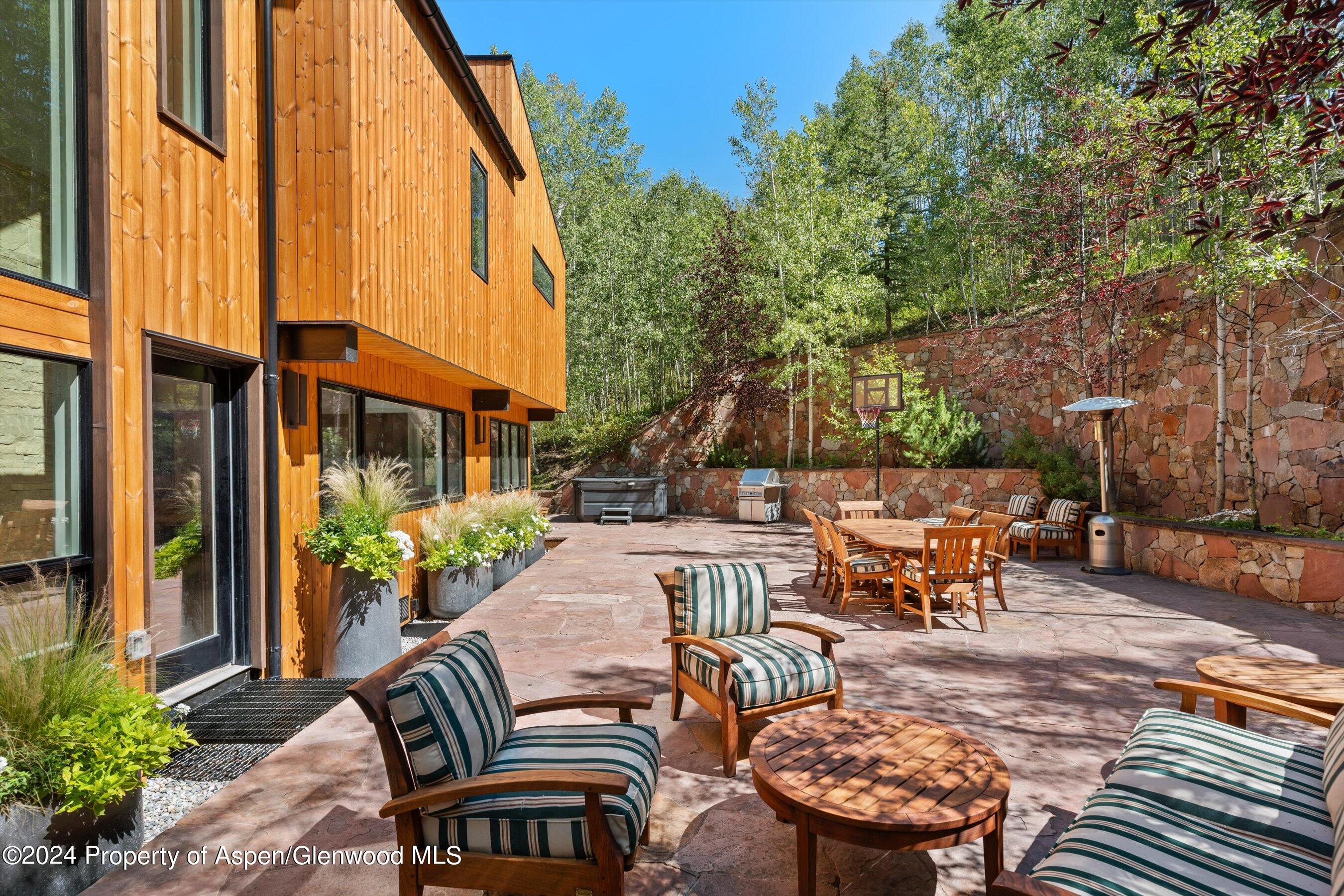 Furnished stone patio beside a wood-sided home, with outdoor dining, a hot tub, and basketball hoop.