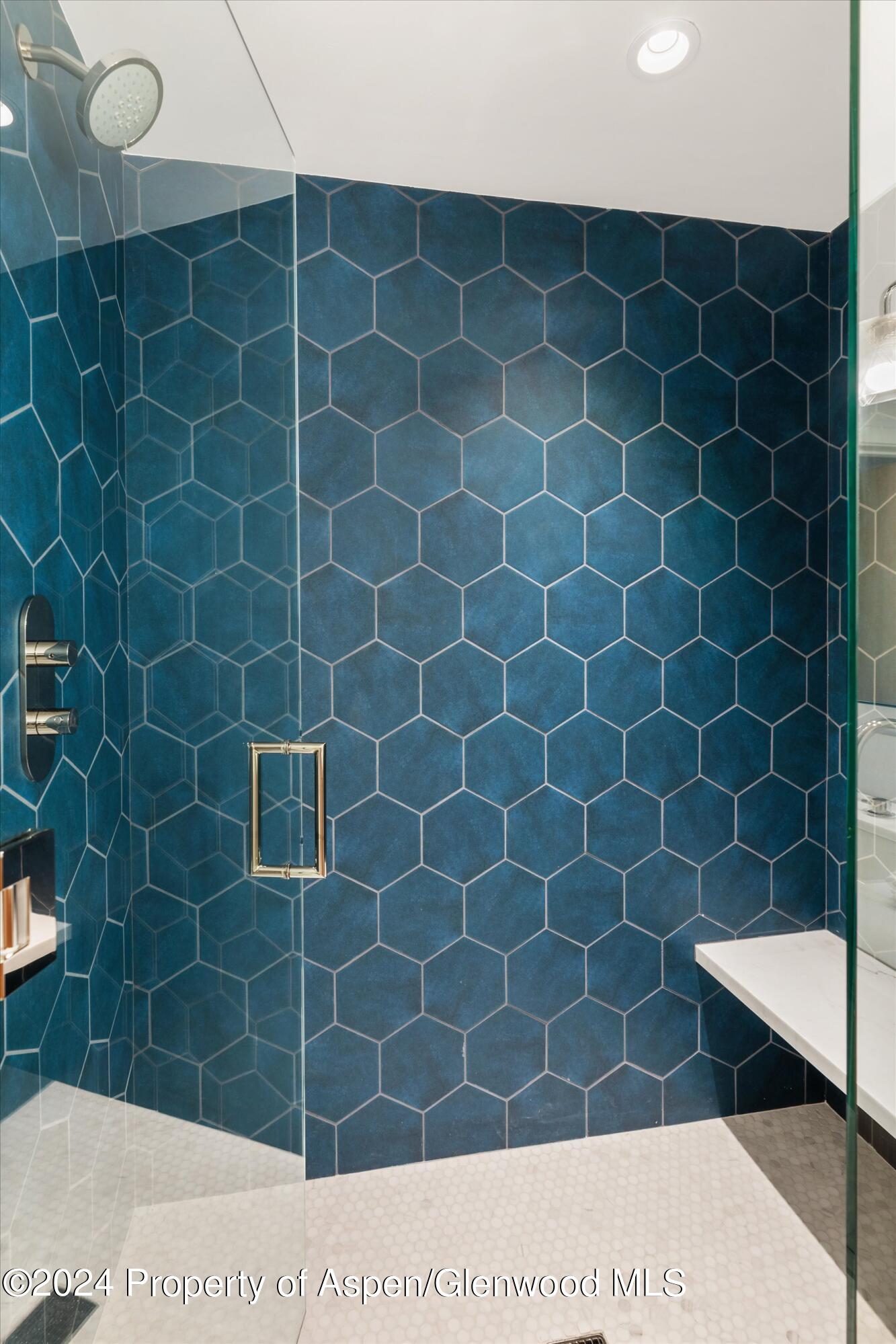 Walk-in shower with deep blue hexagonal tile, glass enclosure, and rainfall showerhead.