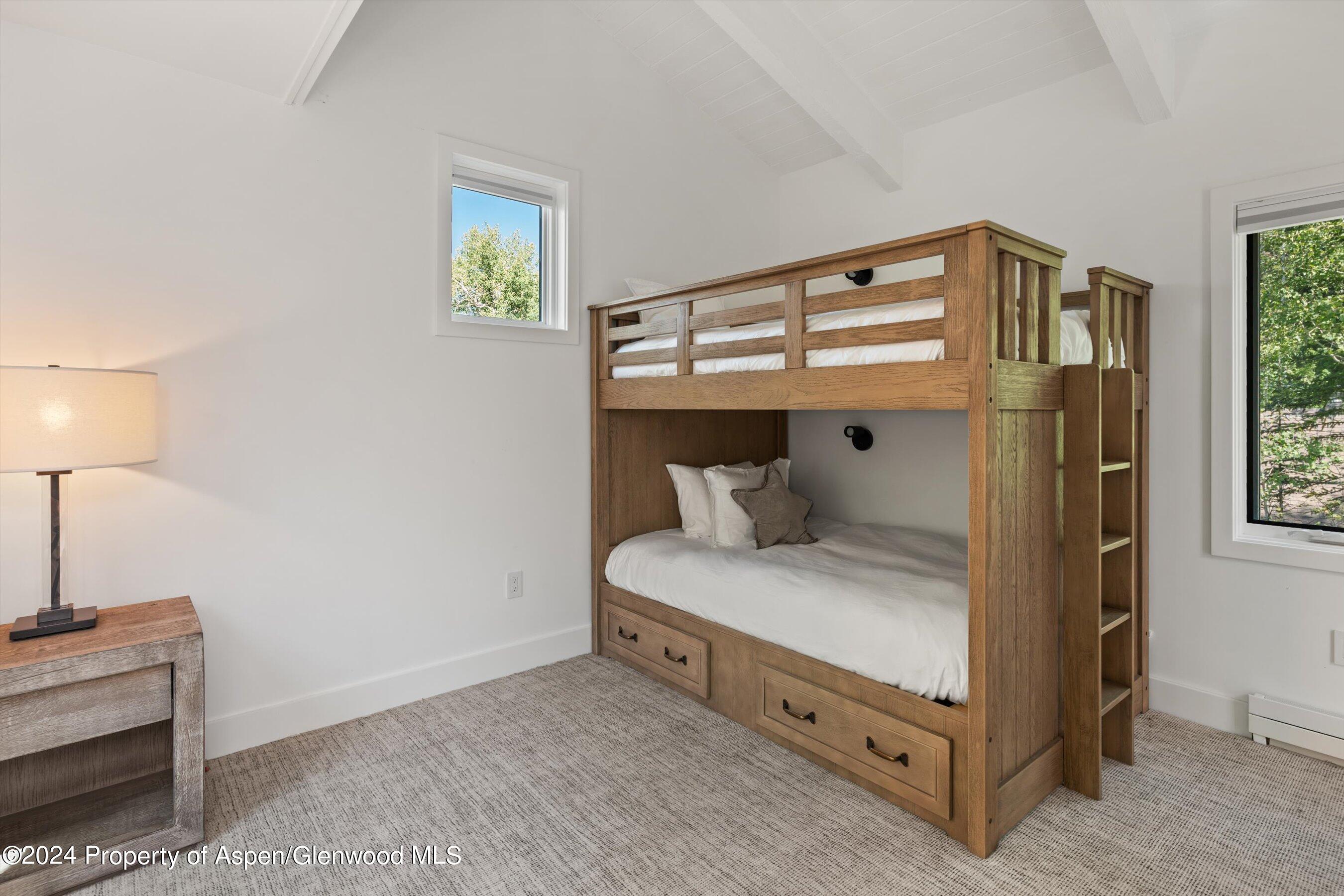 Bedroom with a wooden bunk bed, built-in drawers, and windows overlooking trees.