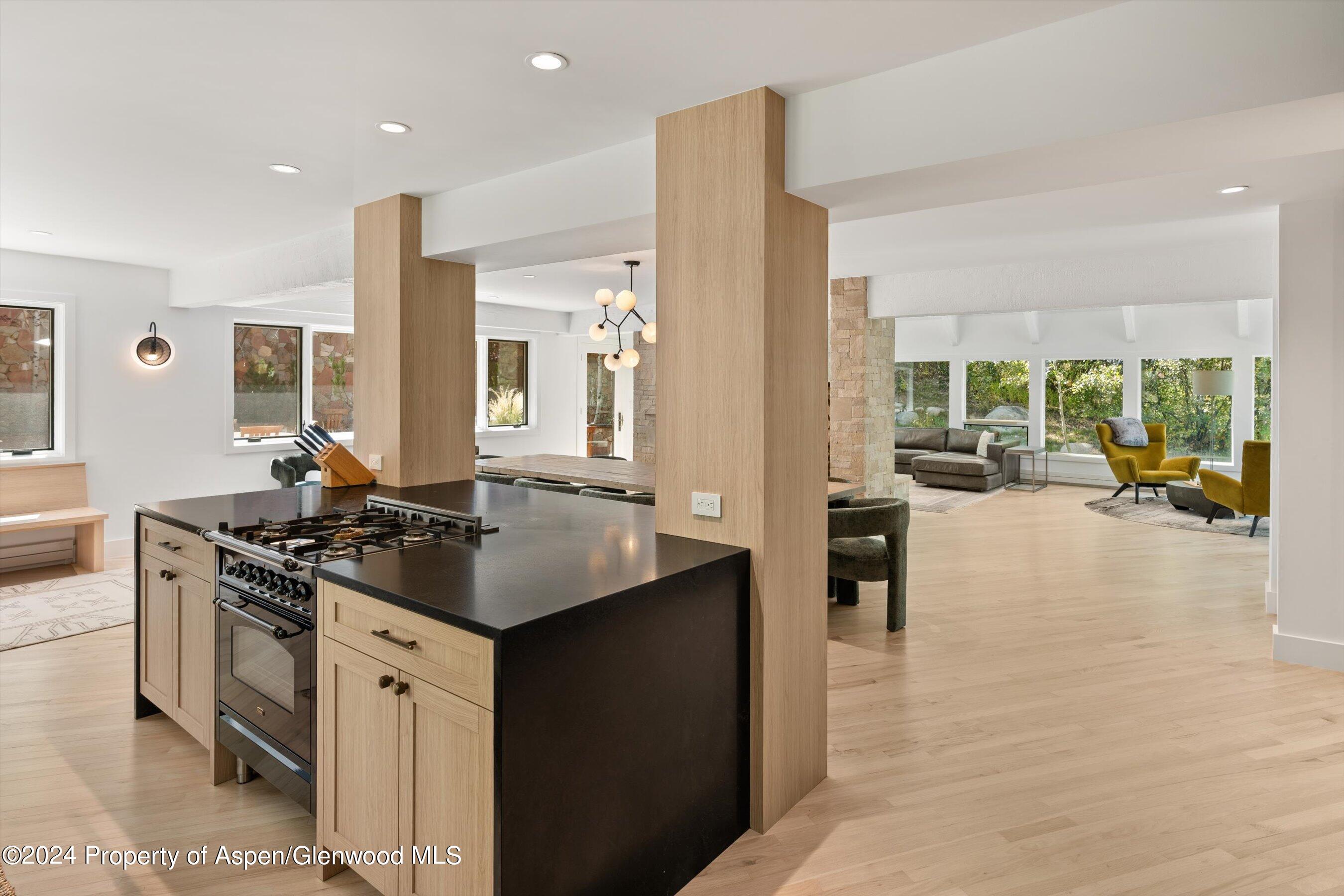 Open kitchen with a black island and gas range, adjoining a bright living room with large windows.
