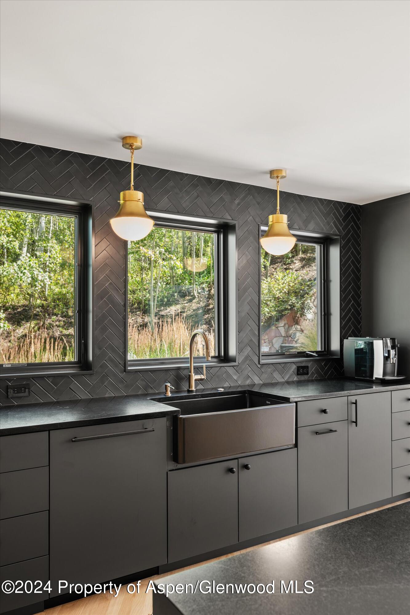 Modern kitchen with a deep farmhouse sink, charcoal herringbone tile, and brass pendant lights.