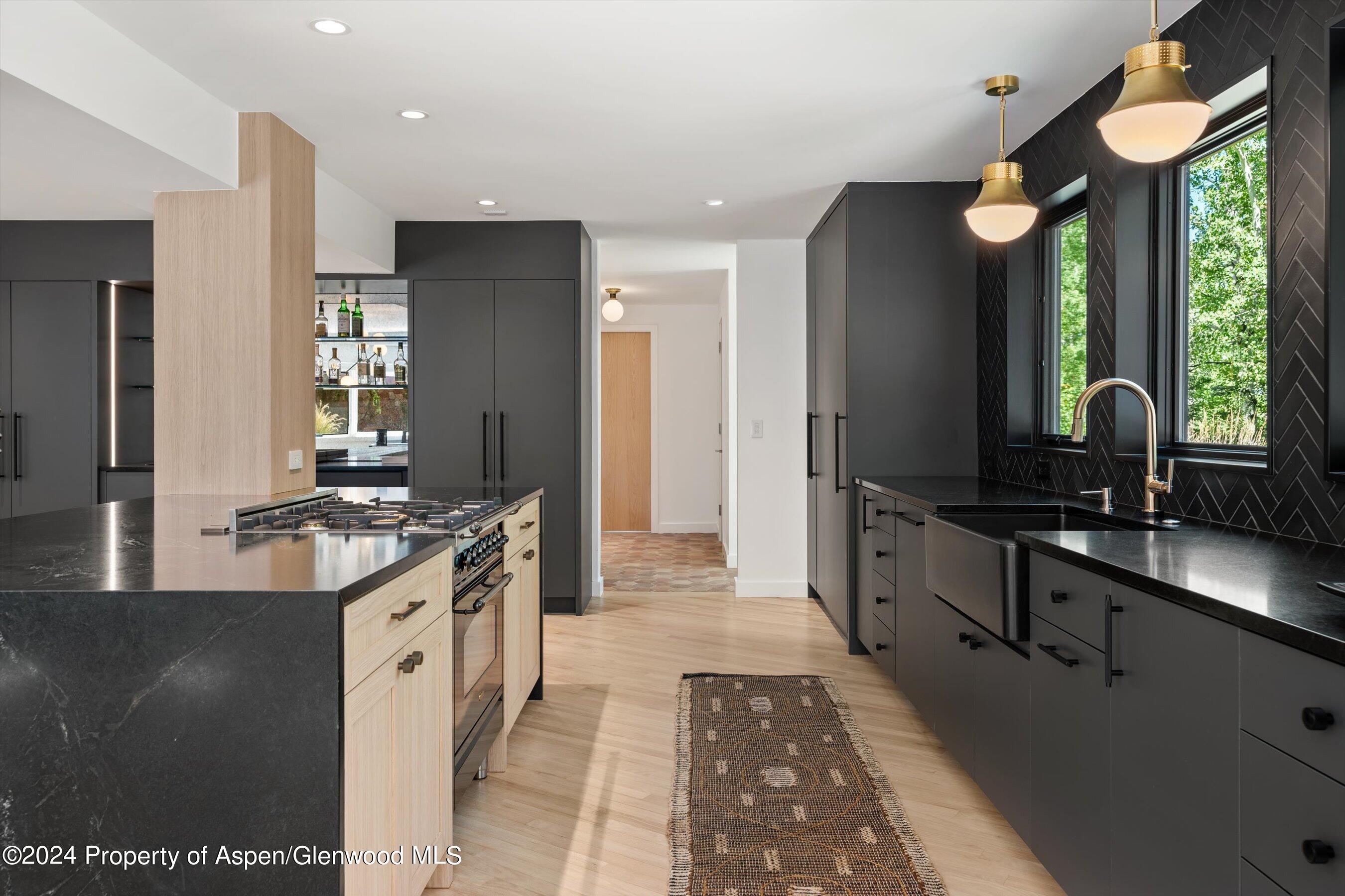 Modern kitchen with dark cabinetry, a light wood island, and windows overlooking trees.