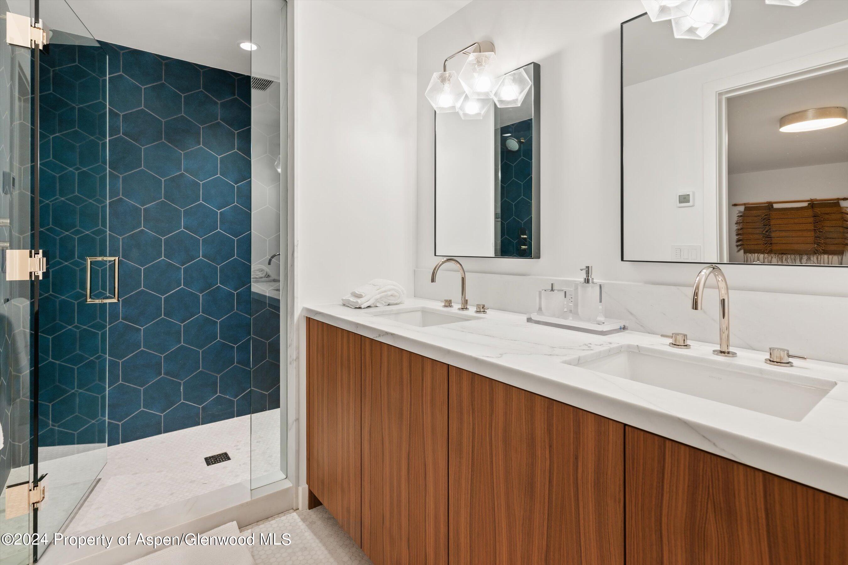 Bathroom with a double-sink wood vanity and glass shower featuring blue hexagonal tile.