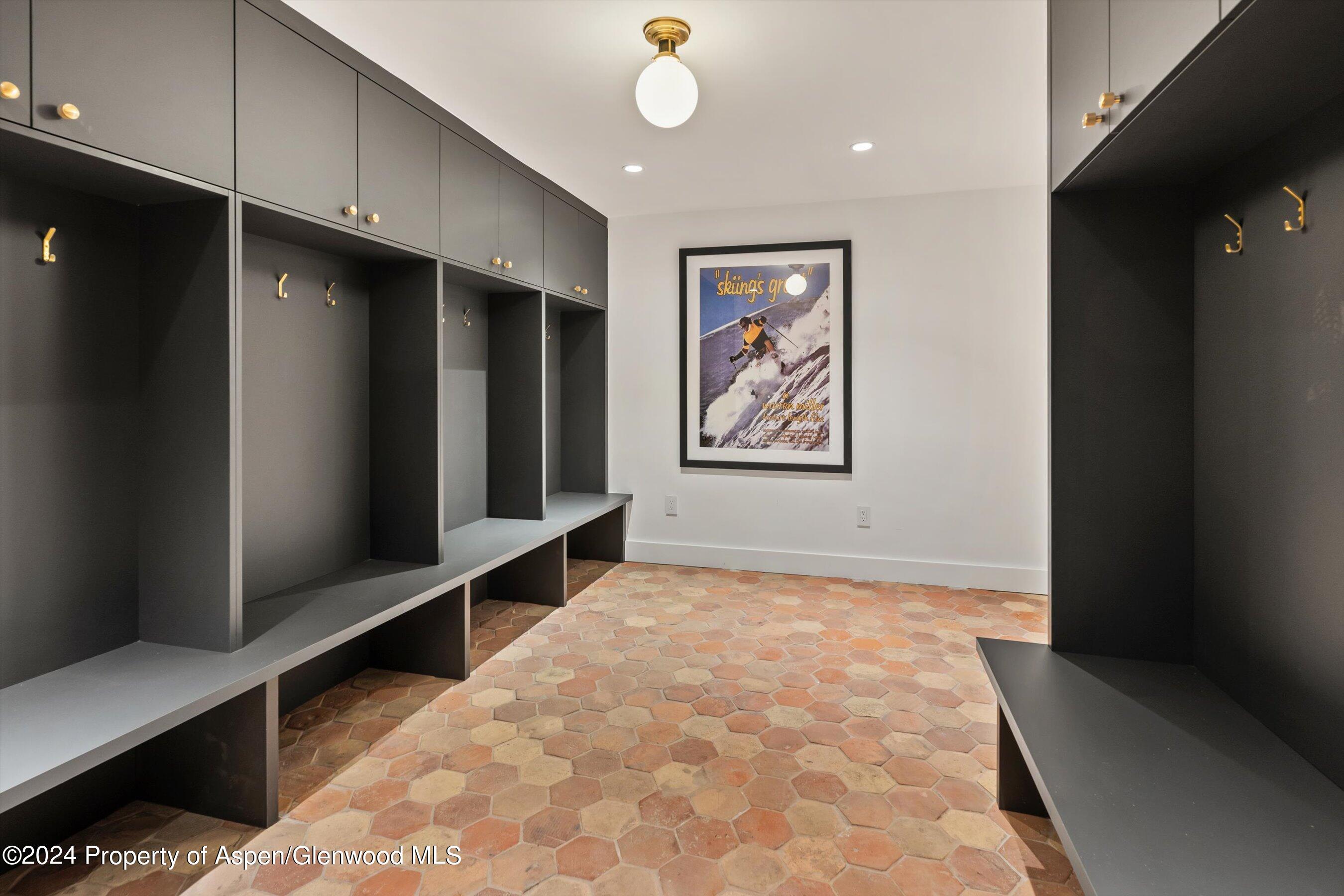 Mudroom with dark built-in cubbies, brass hooks, bench seating, and terracotta tile floor.