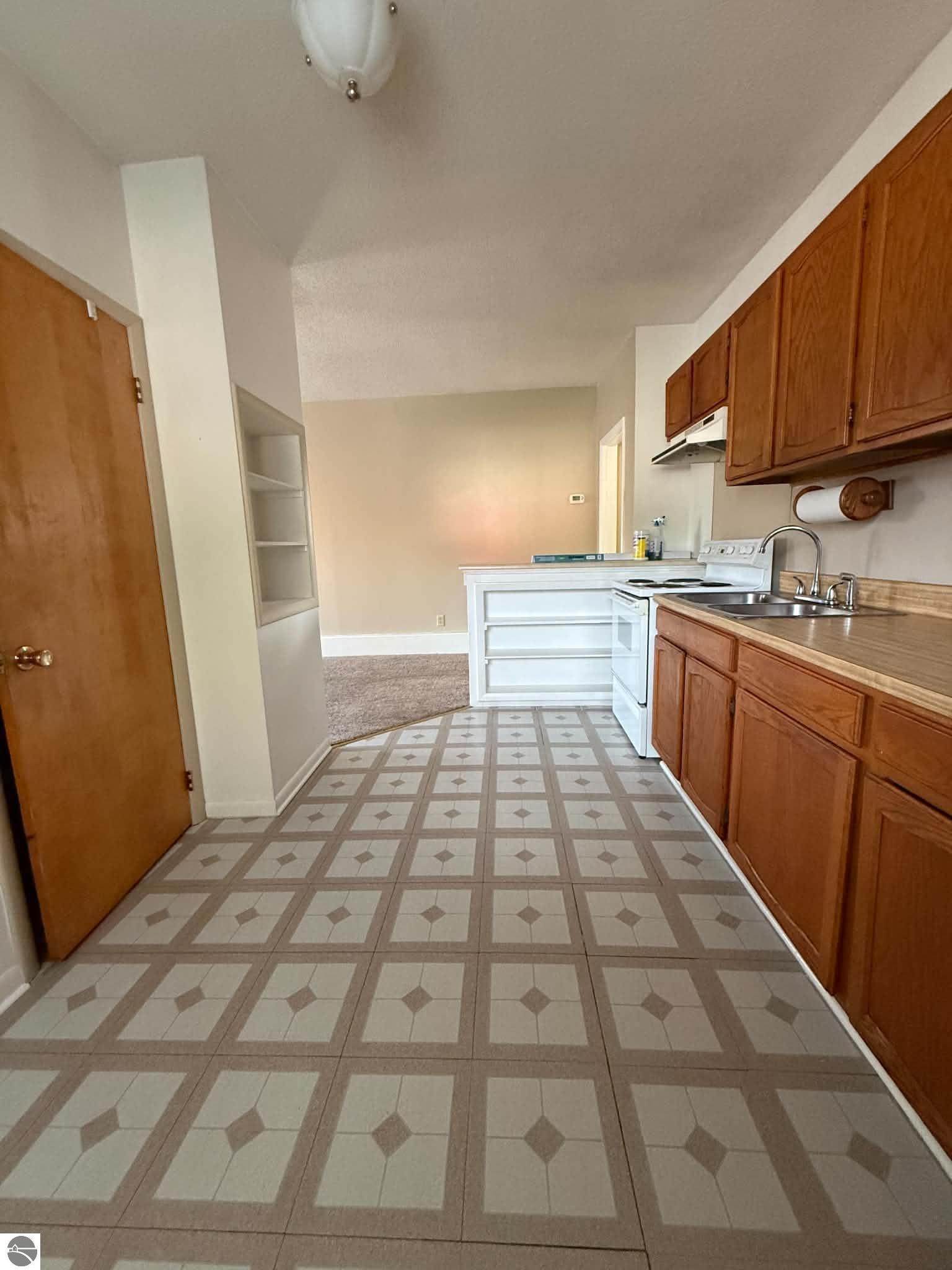 Kitchen with wood cabinets, a double-basin sink, white electric range, and patterned tile floor.