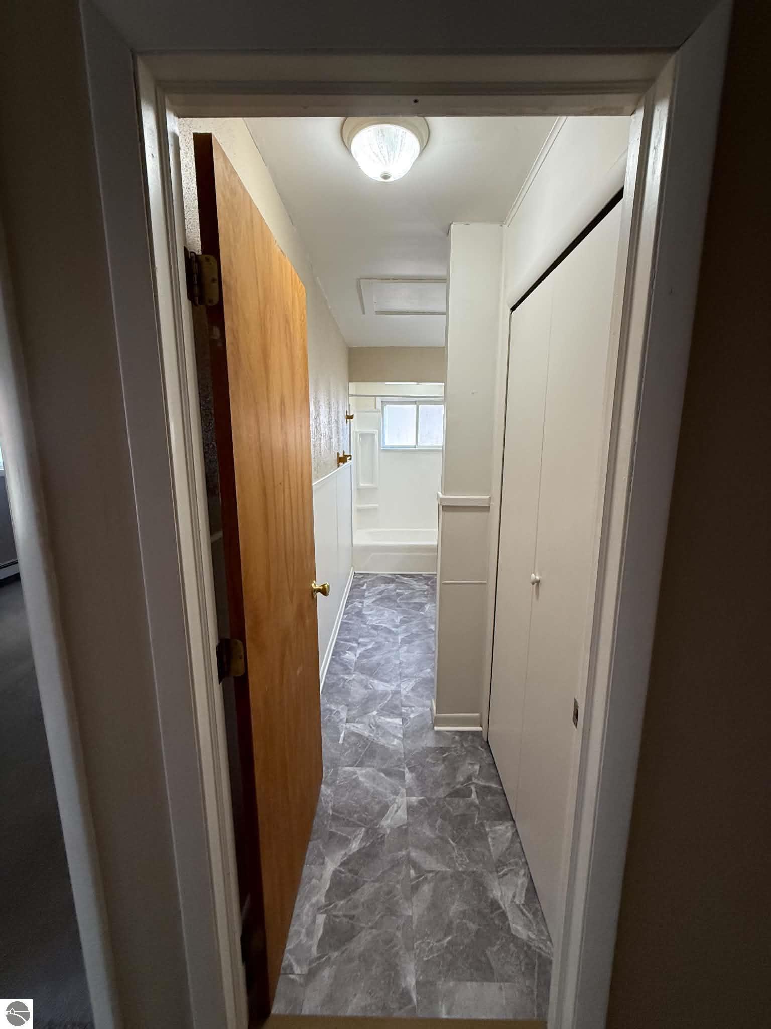Narrow passage with gray tile flooring, white built-in cabinets, and a window at the far end.
