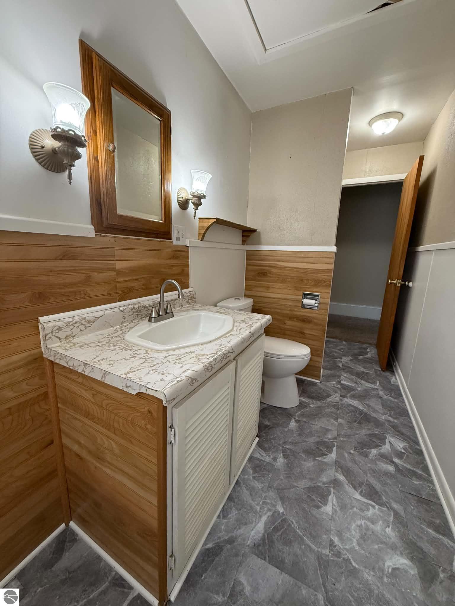 Bathroom with wood-paneled walls, a marble-pattern vanity counter, and gray tile flooring.