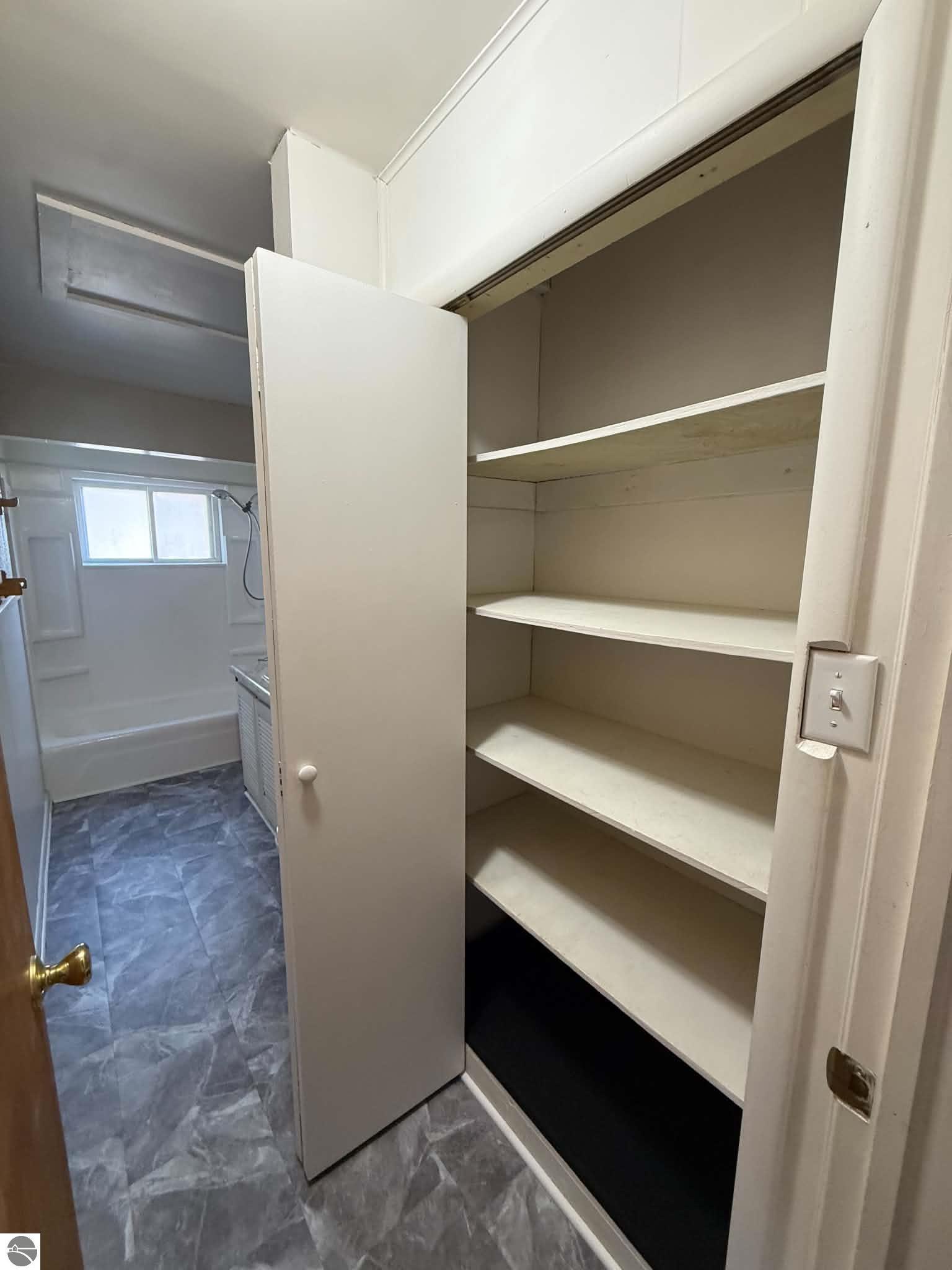 Open built-in linen closet with empty shelves beside a bathroom tub and shower.