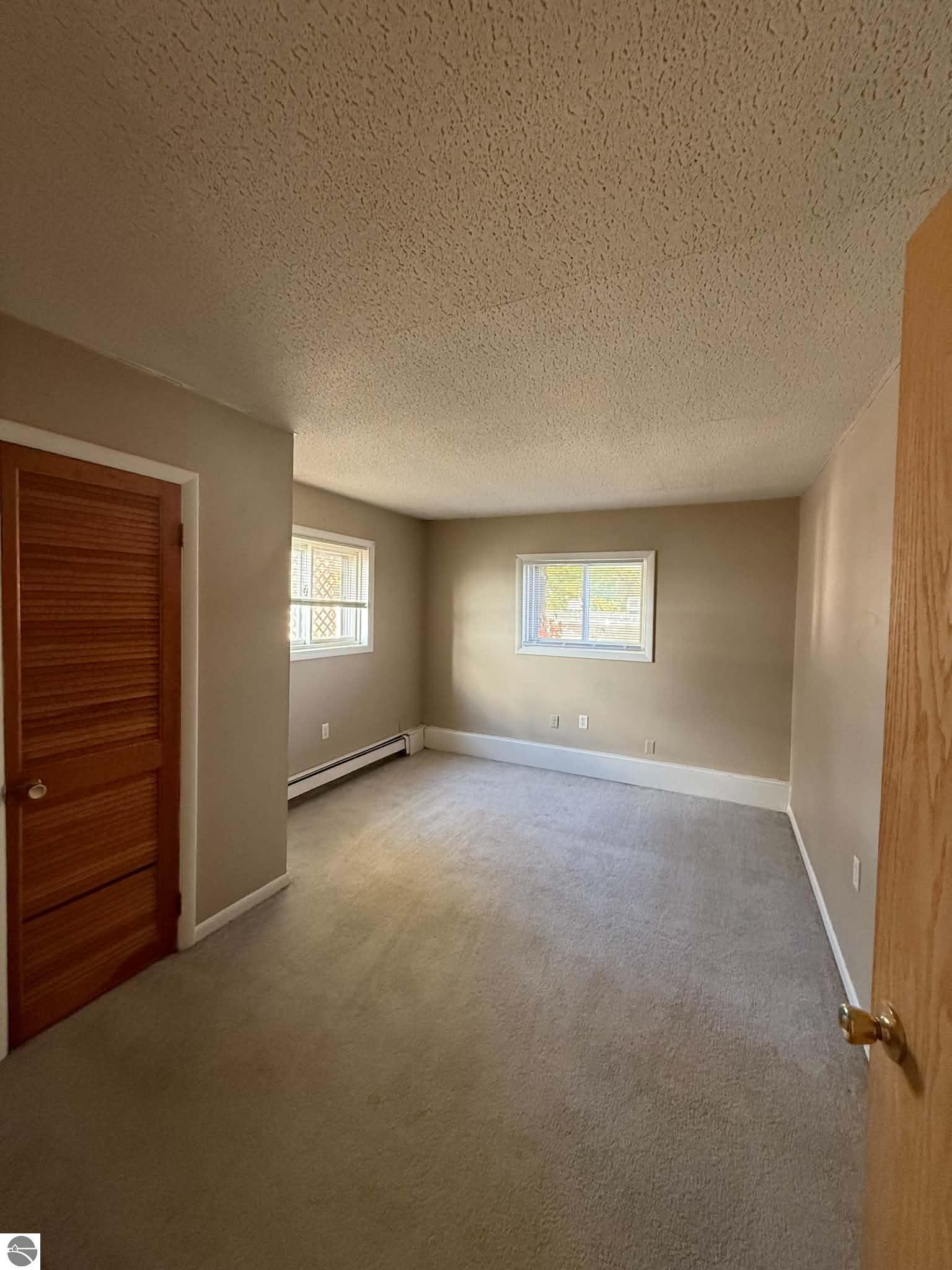 Empty bedroom with gray carpet, two windows, and a wooden louvered closet door.