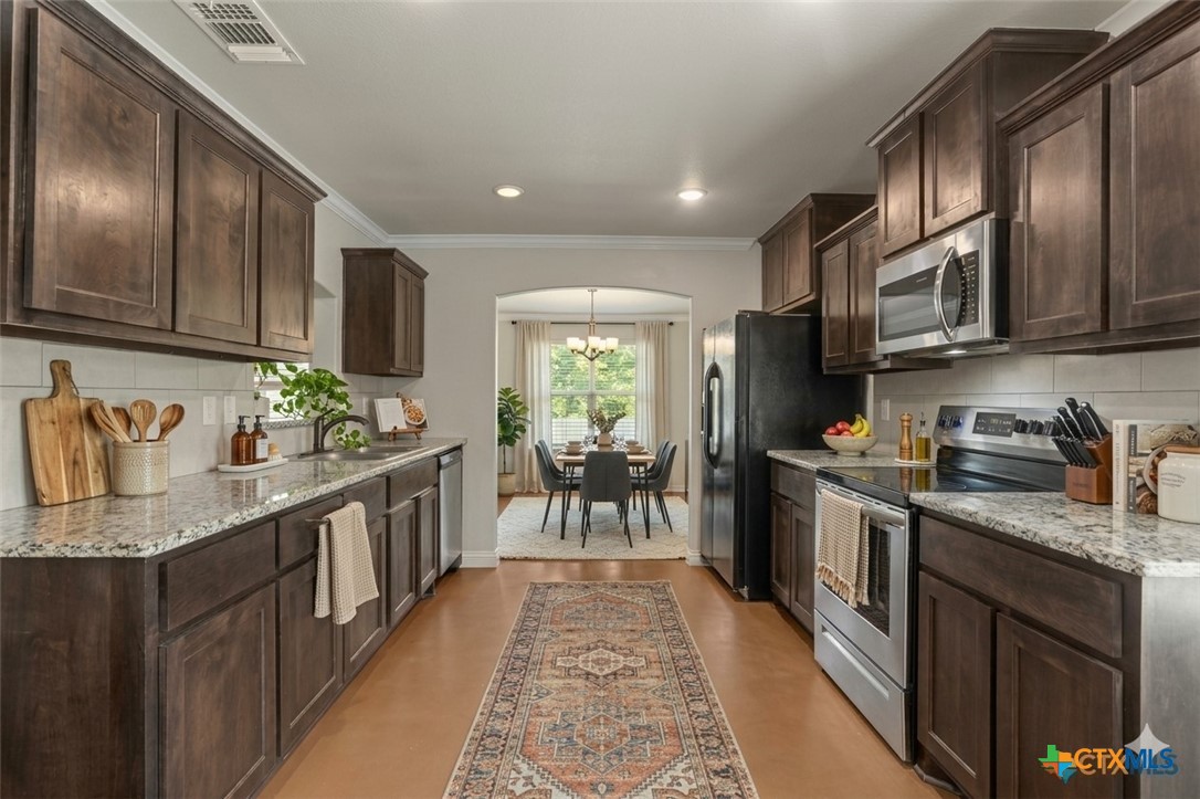 Kitchen with dark wood cabinets, granite counters, stainless steel appliances, and a view into the dining area.
