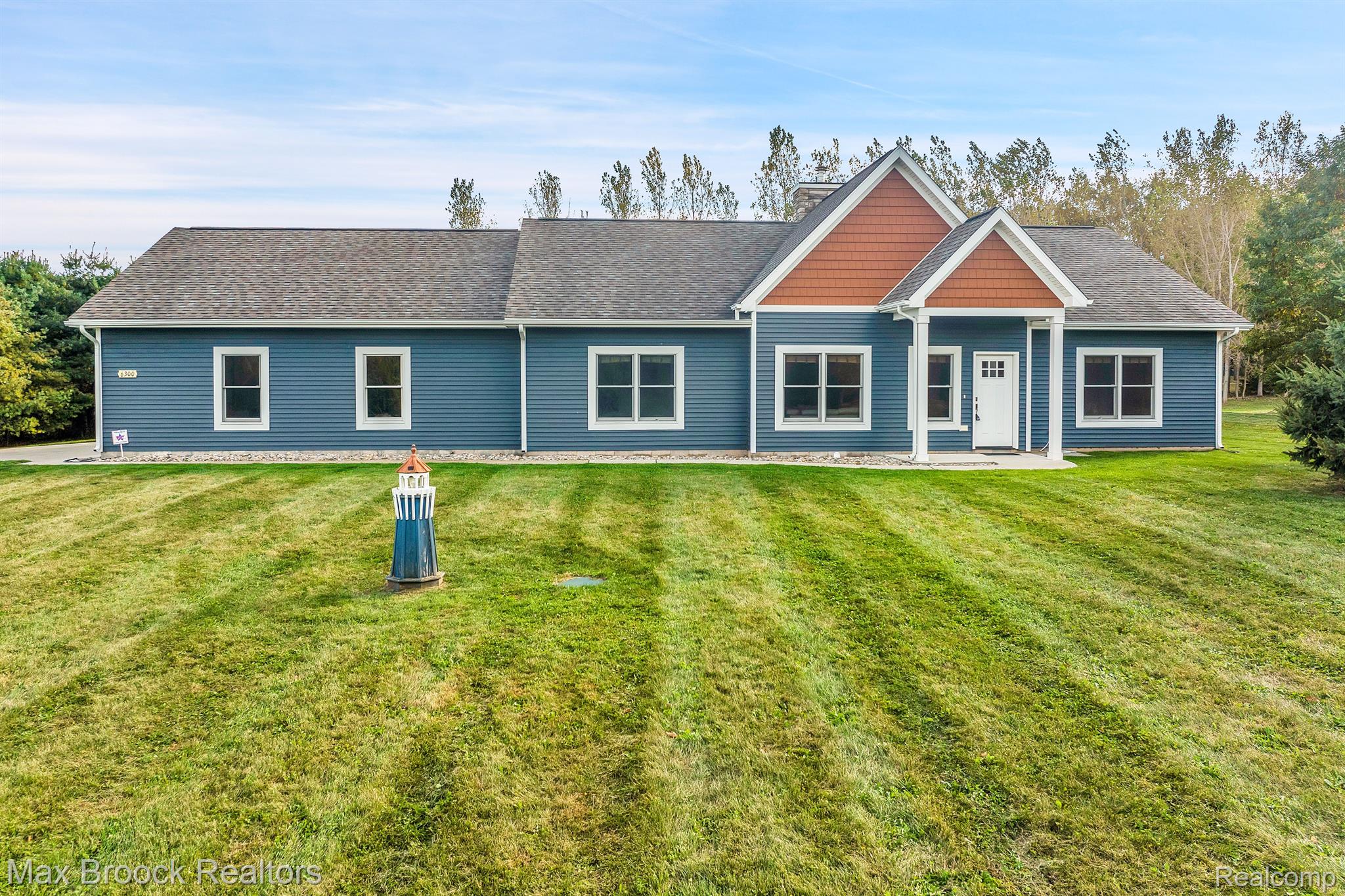 Blue single-story home with twin reddish gables and a lighthouse lawn ornament.