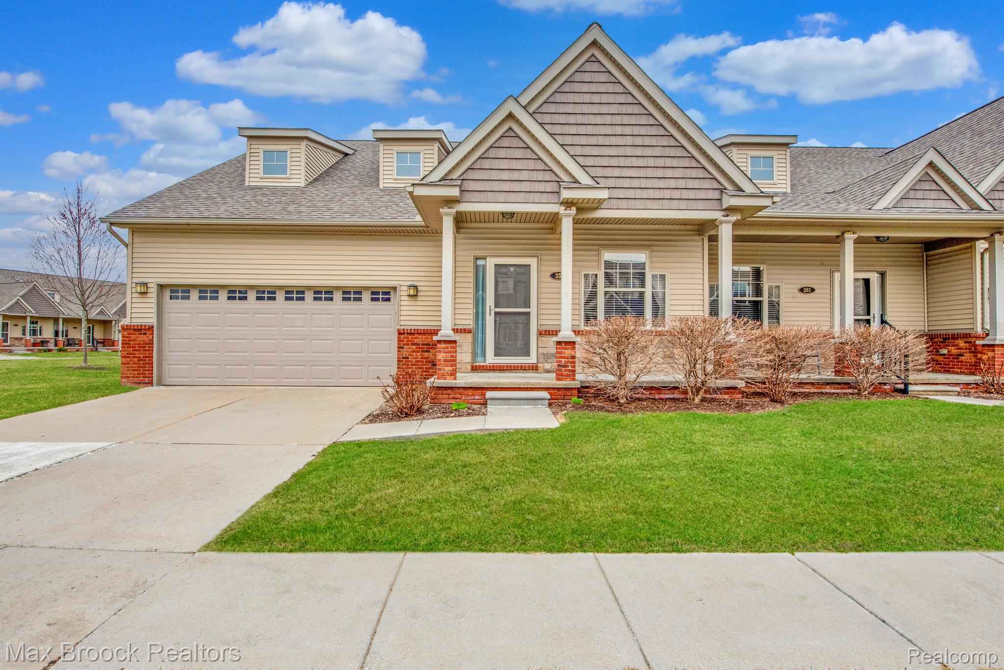 Beige townhouse with a prominent front gable, covered porch, two-car garage, and broad driveway.
