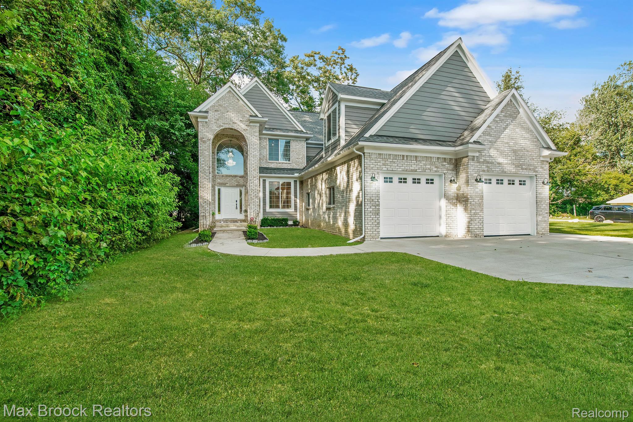 Two-story brick and gray-sided home with an arched entry, double garage, and broad green lawn.