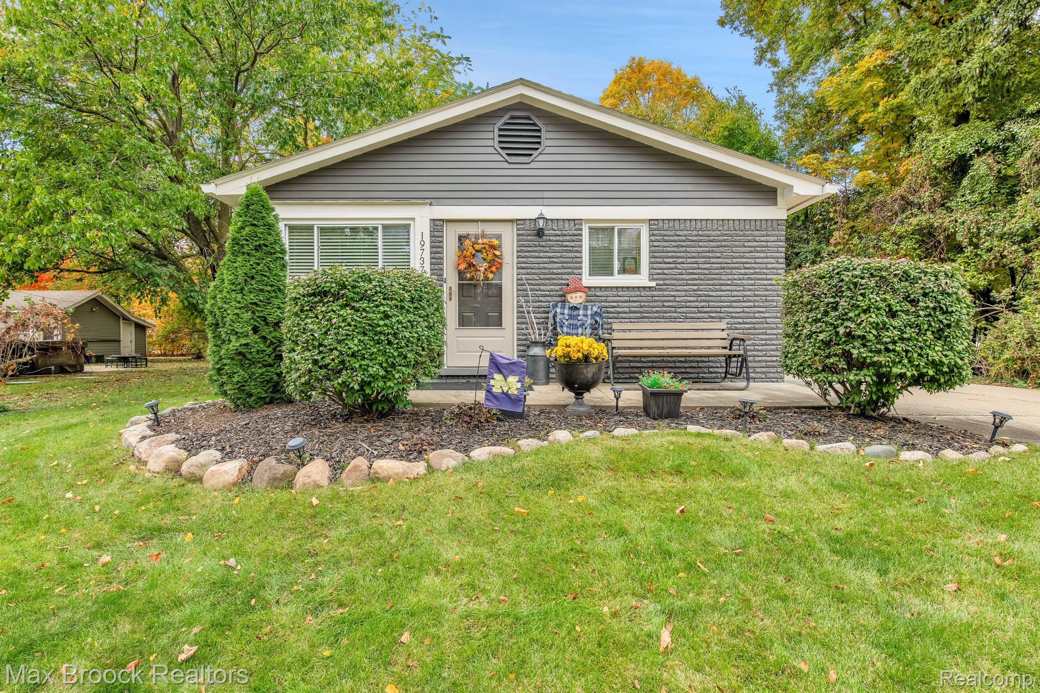 Gray single-story home with a stone facade, fall wreath, porch bench, and landscaped lawn.