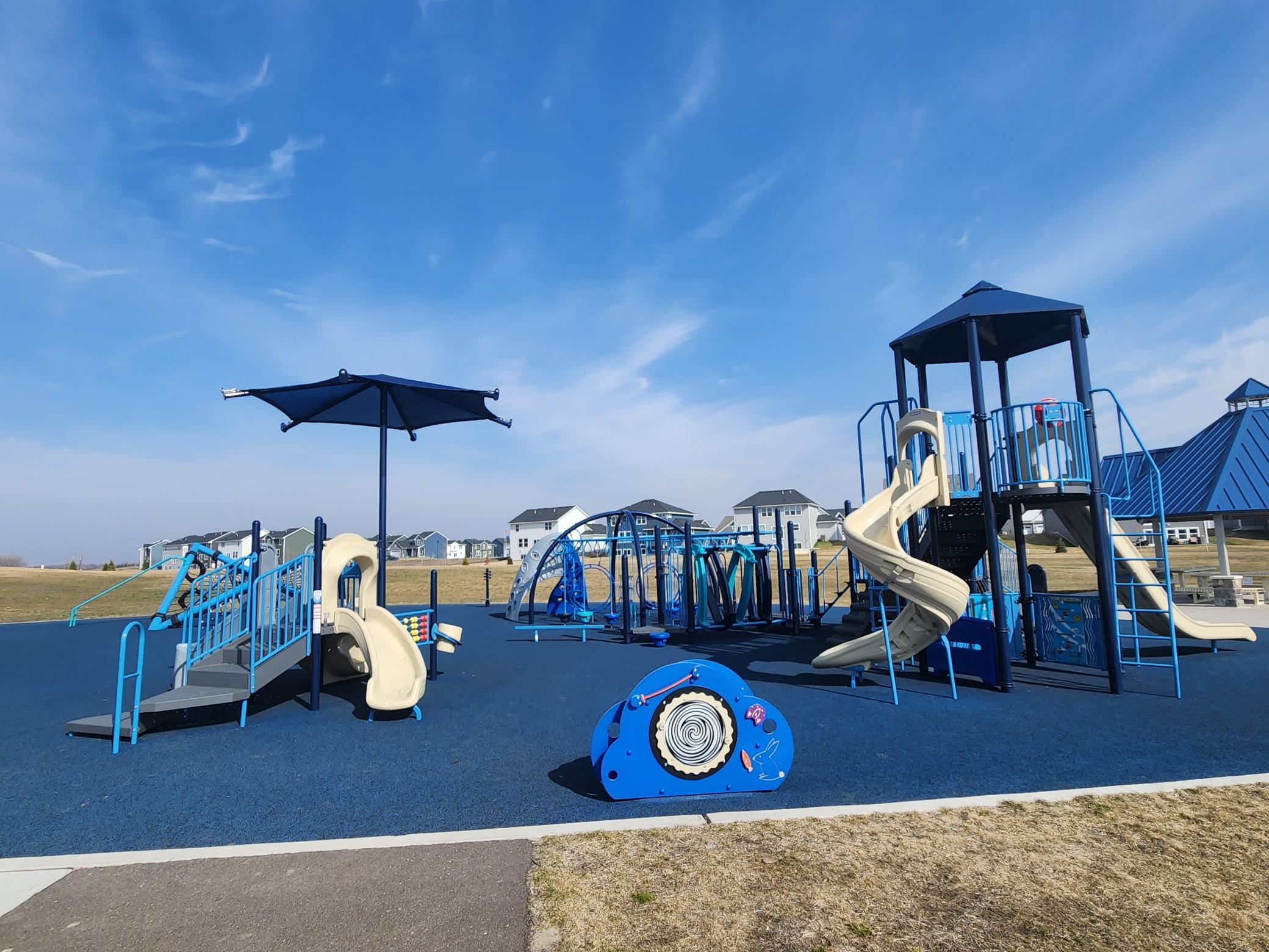 Community playground with climbing equipment, cream slides, and a shade umbrella.