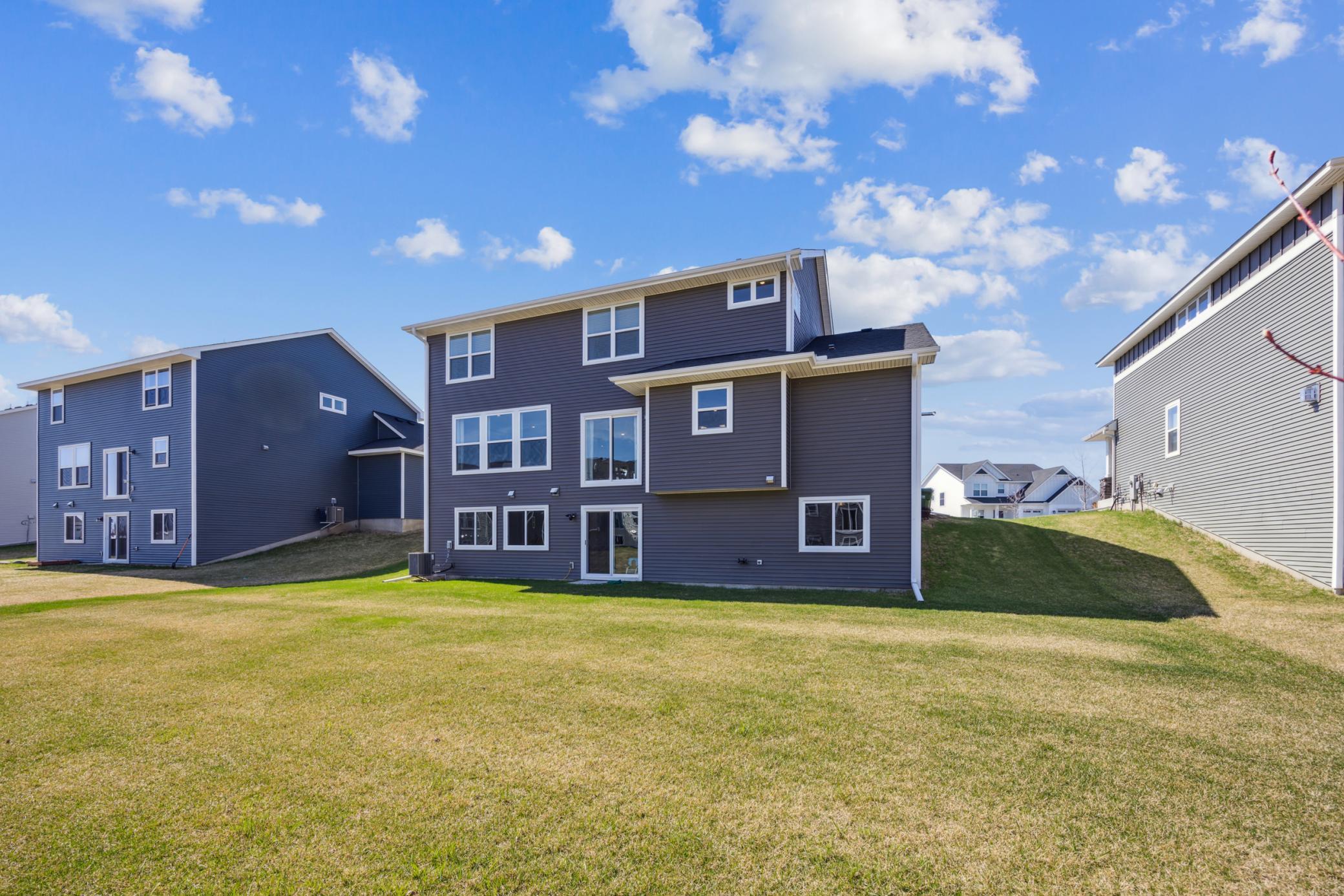 Rear of a two-story gray house overlooking a broad sloping lawn between neighboring homes.