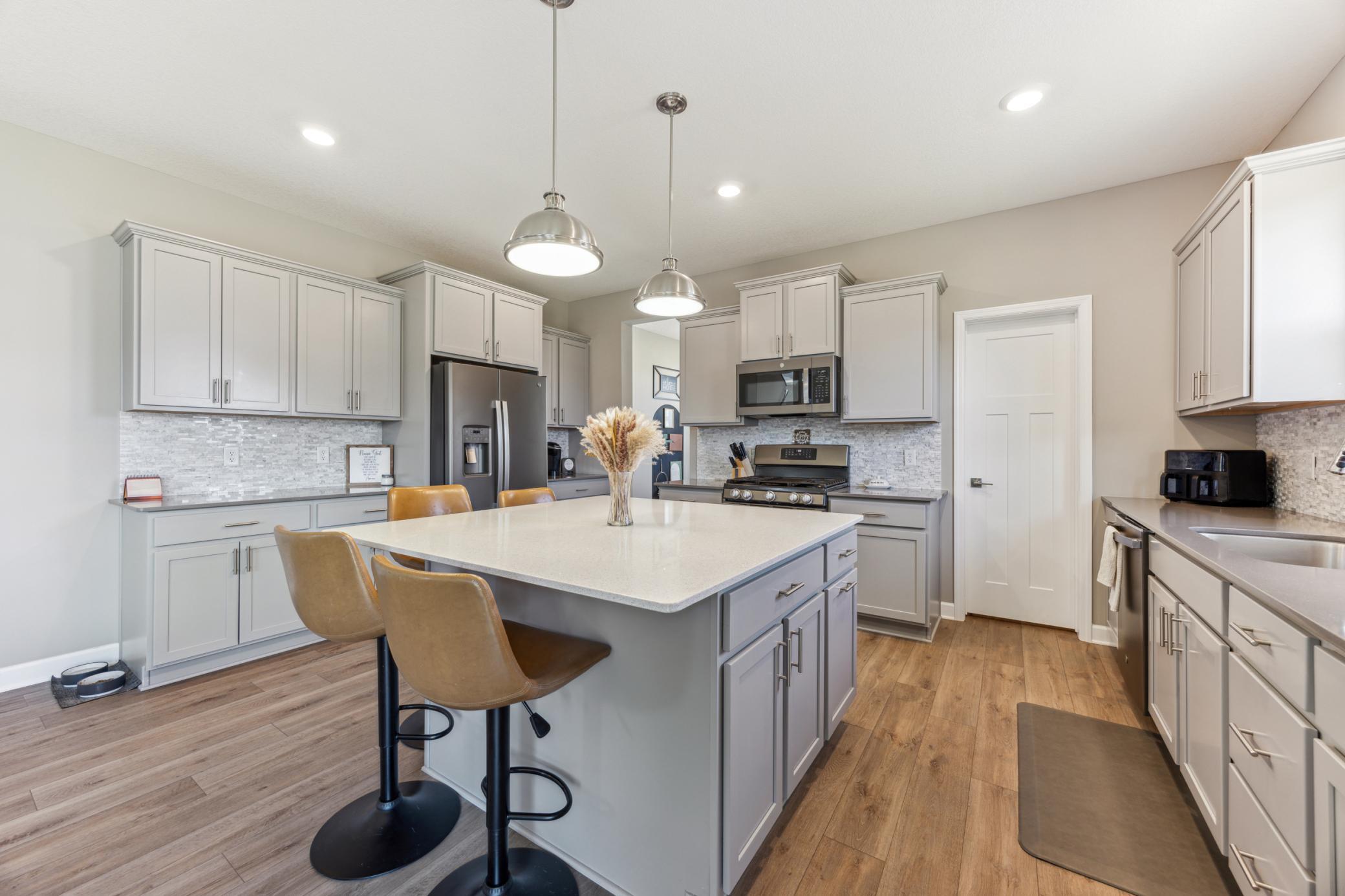 Kitchen with gray cabinets, stainless appliances, and a large island with bar stools.