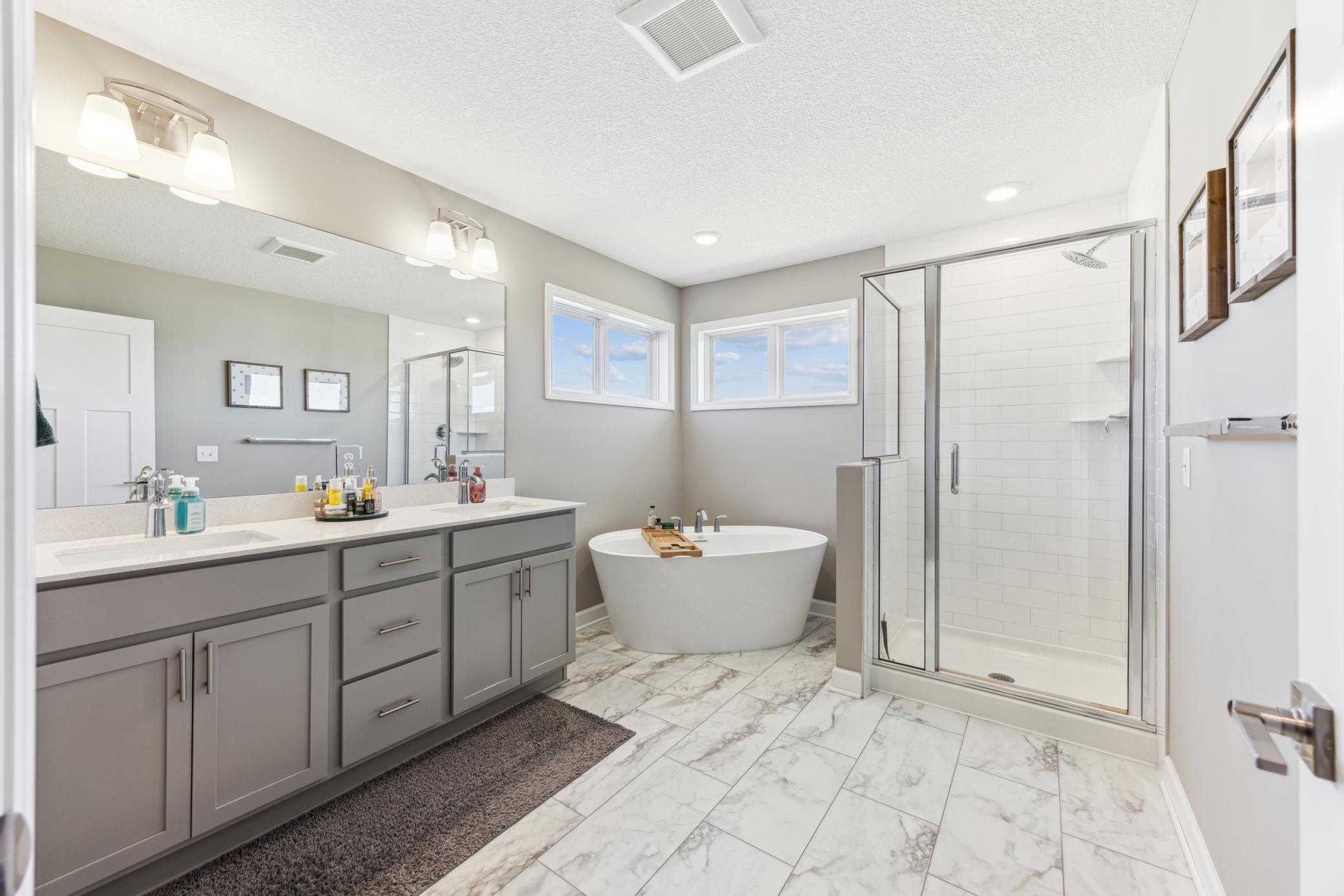 Primary bathroom with gray double vanity, freestanding tub, and glass-enclosed tile shower.