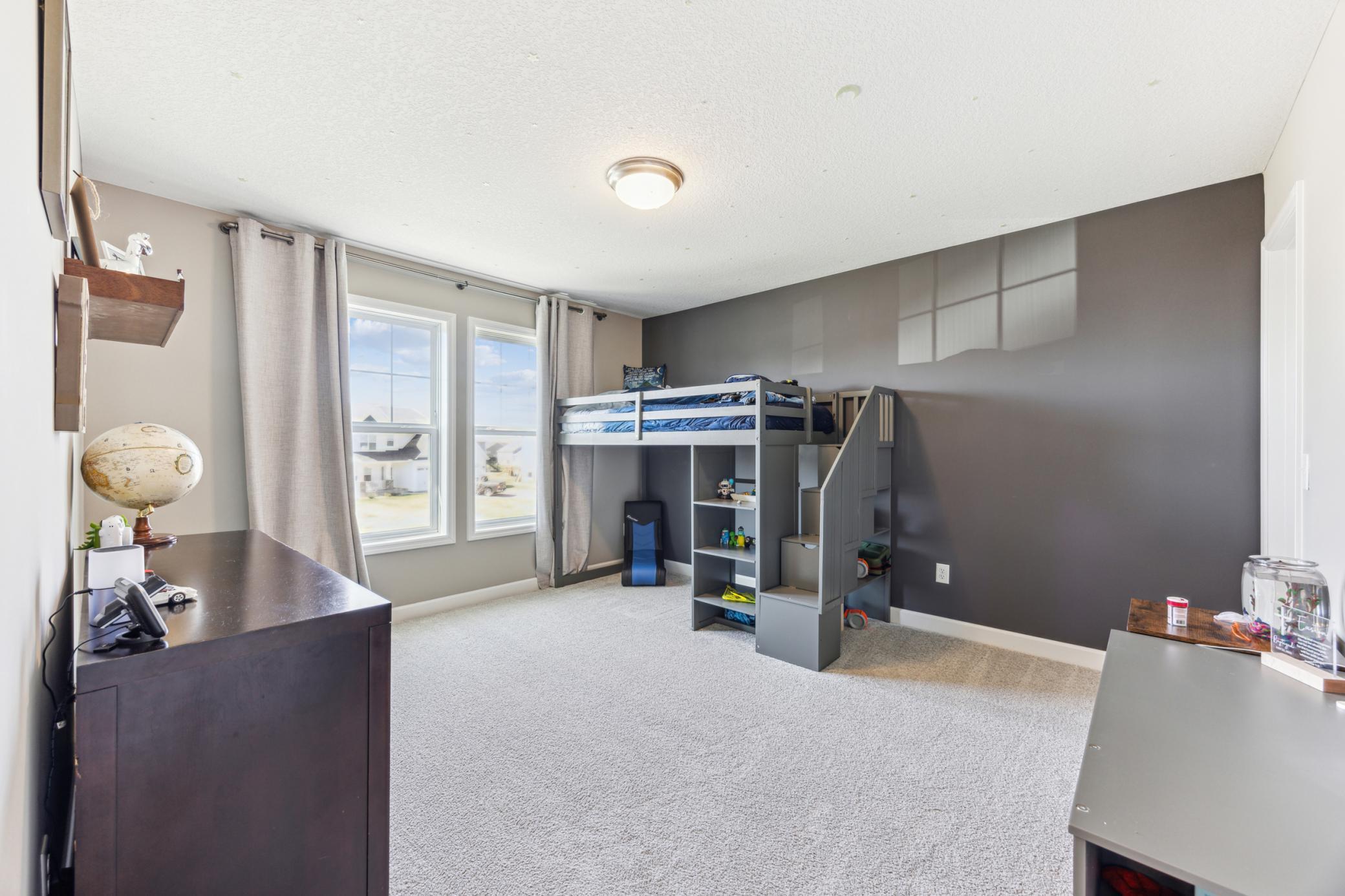 Bedroom with gray loft bunk bed and built-in stairs, two windows, and light carpet.