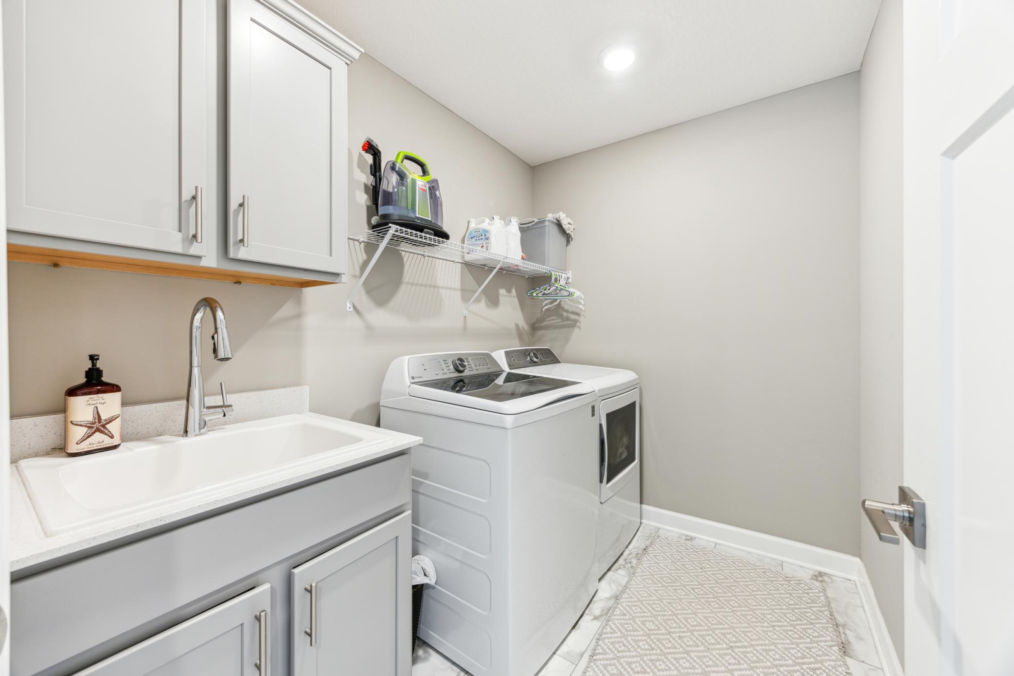 Laundry room with a utility sink, gray cabinets, and white washer and dryer.