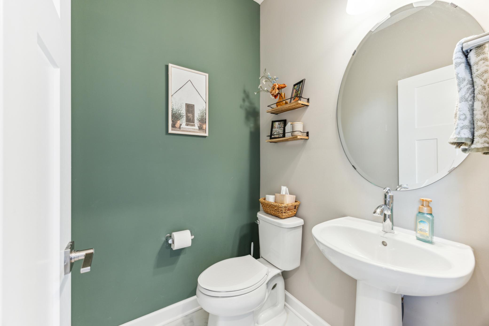 Bathroom with a white pedestal sink, round mirror, and deep green accent wall.