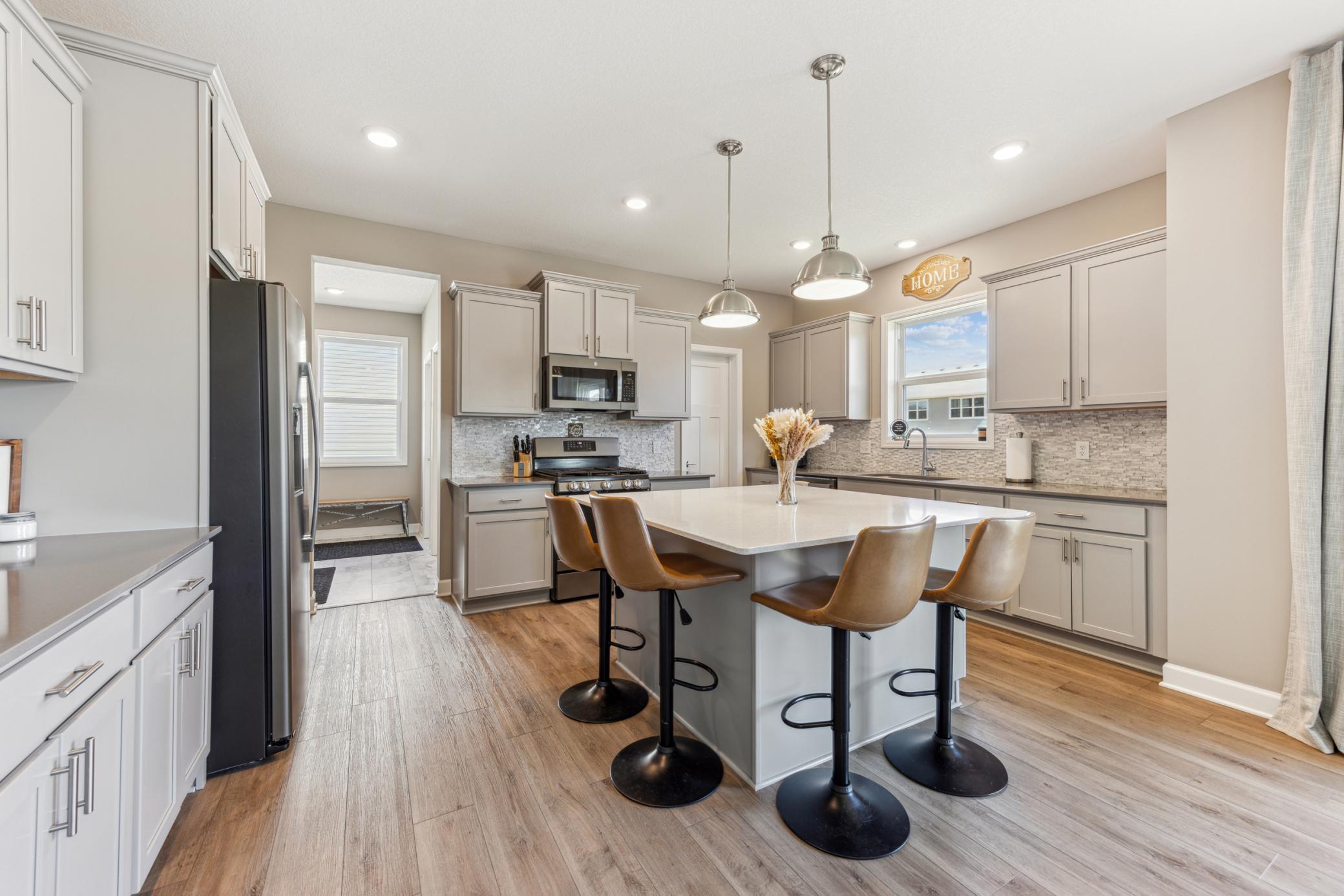 Kitchen with gray cabinets, stainless steel appliances, and a large island with four bar stools.