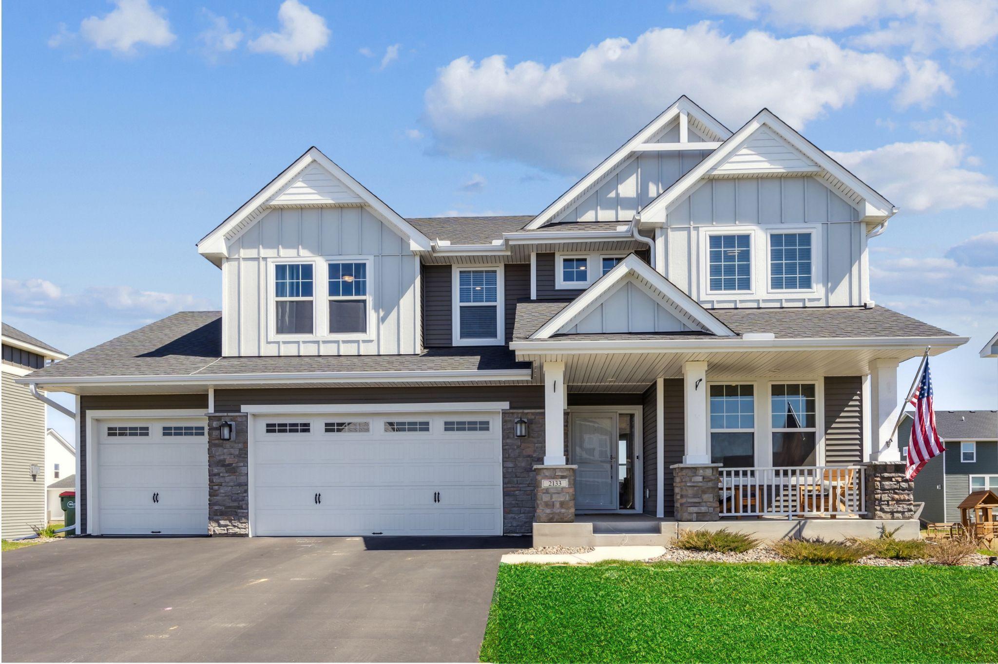 Two-story gray-and-white house with a two-car garage, covered porch, and American flag.
