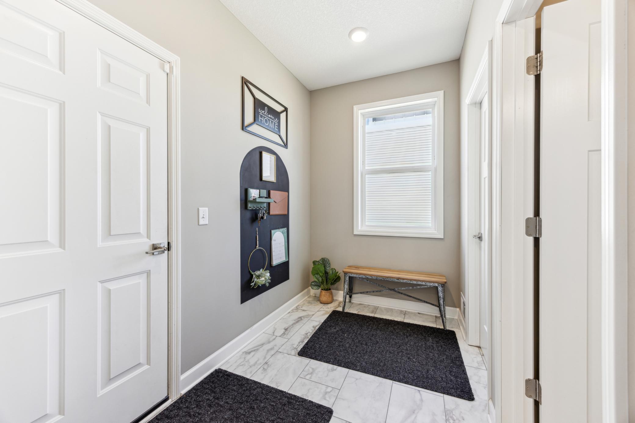 Entry foyer with marble-look tile, a wooden bench, and a wall-mounted key organizer.