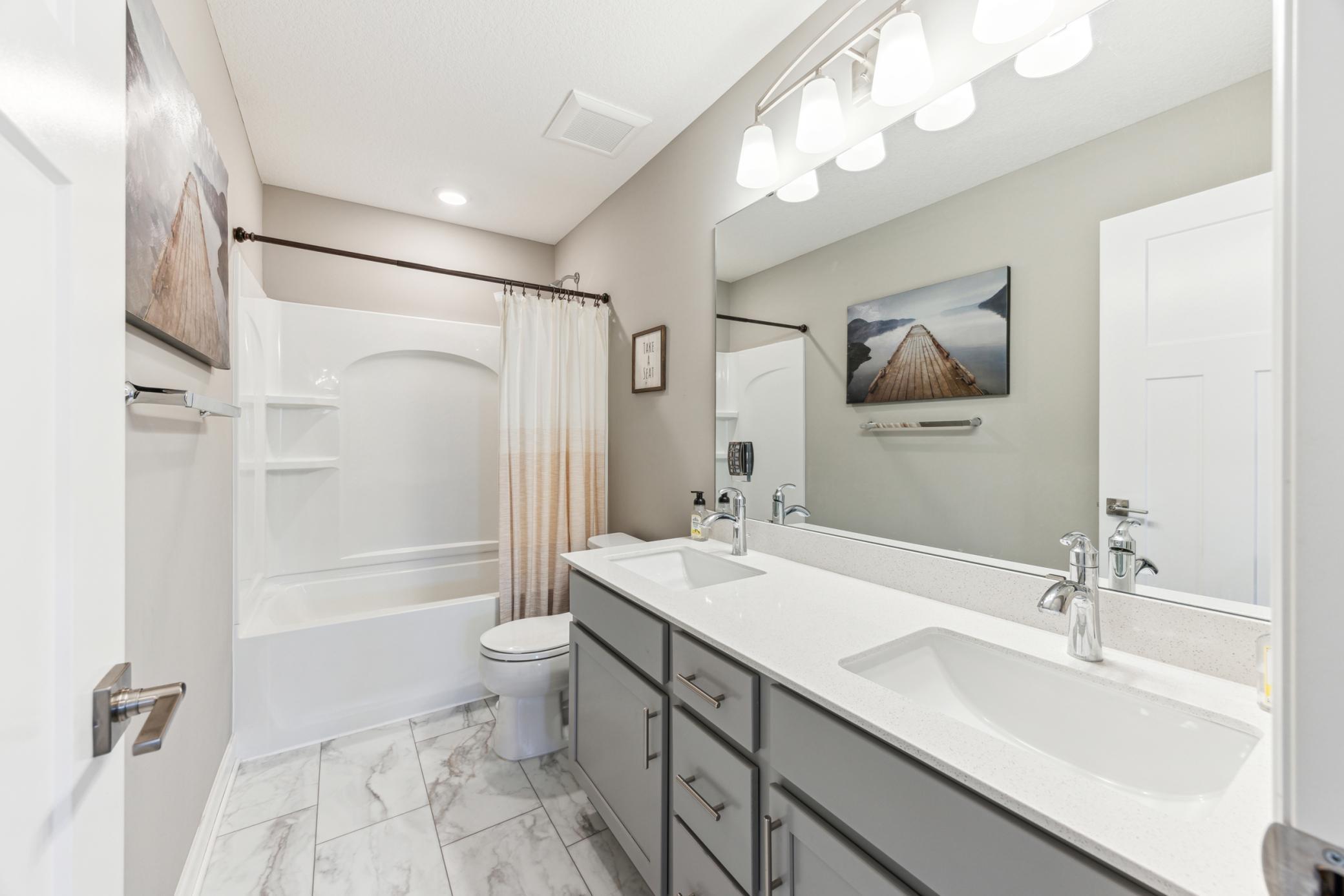 Bathroom with a white tub and shower beside a gray double vanity with two sinks.