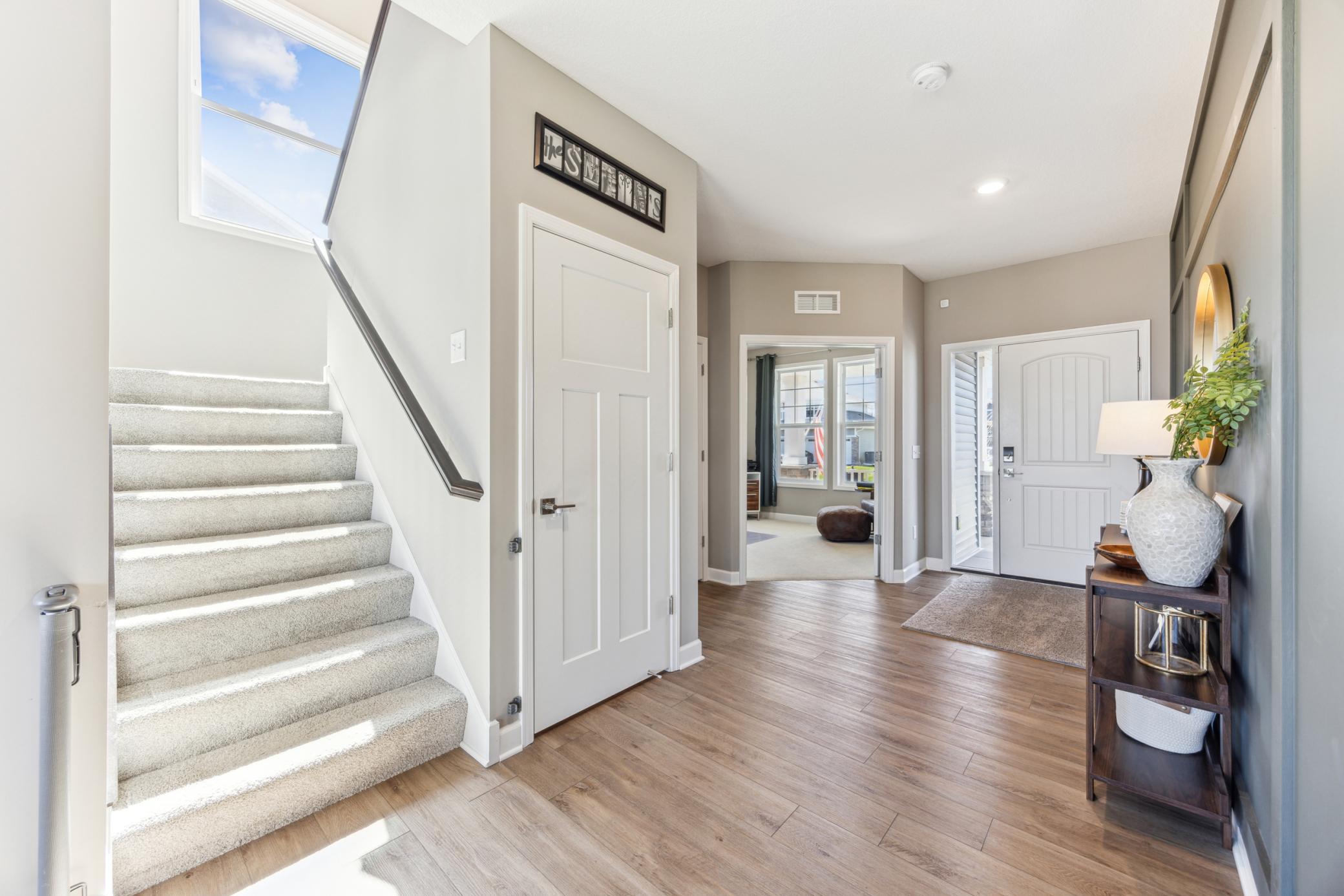 Entry foyer with carpeted staircase, tall window, wood-look floors, and a console table beside the front door.