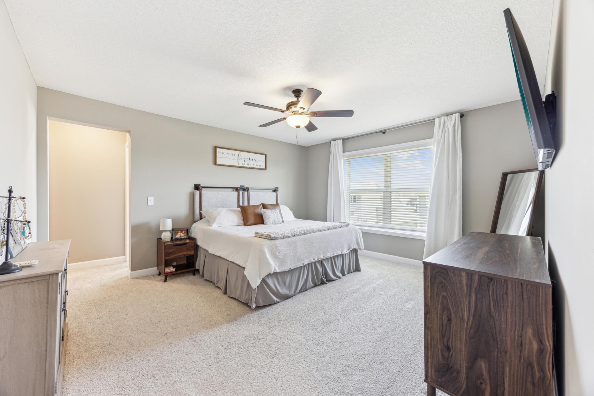 Furnished bedroom with a white bed, gray walls, and a large curtained window.