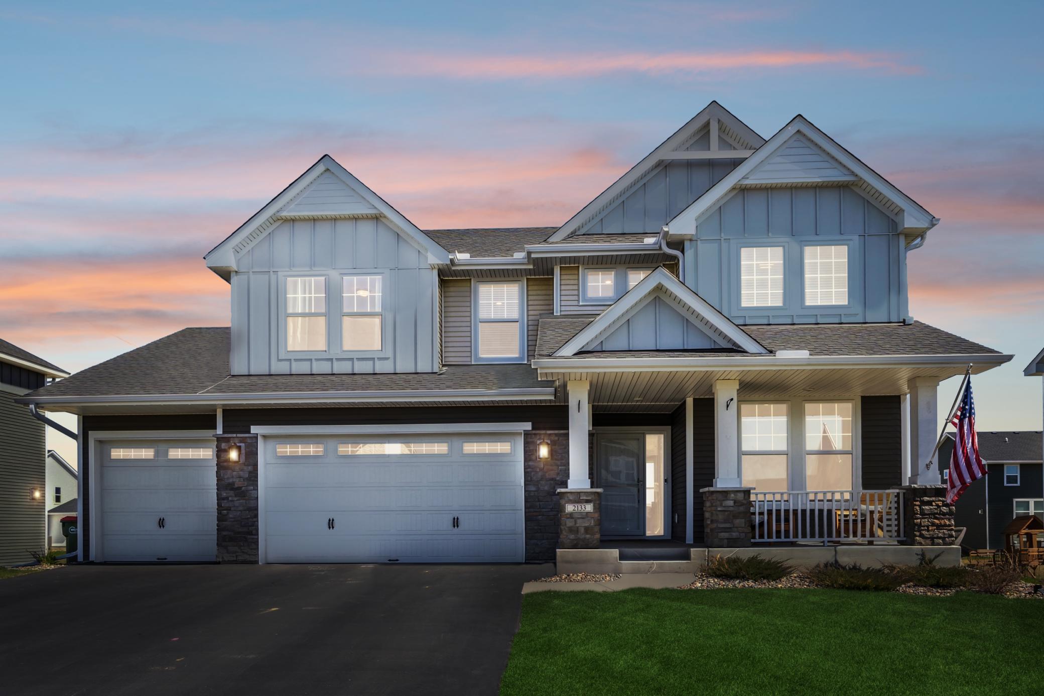 Two-story blue house with multiple gables, a two-car garage, and a covered porch at dusk.