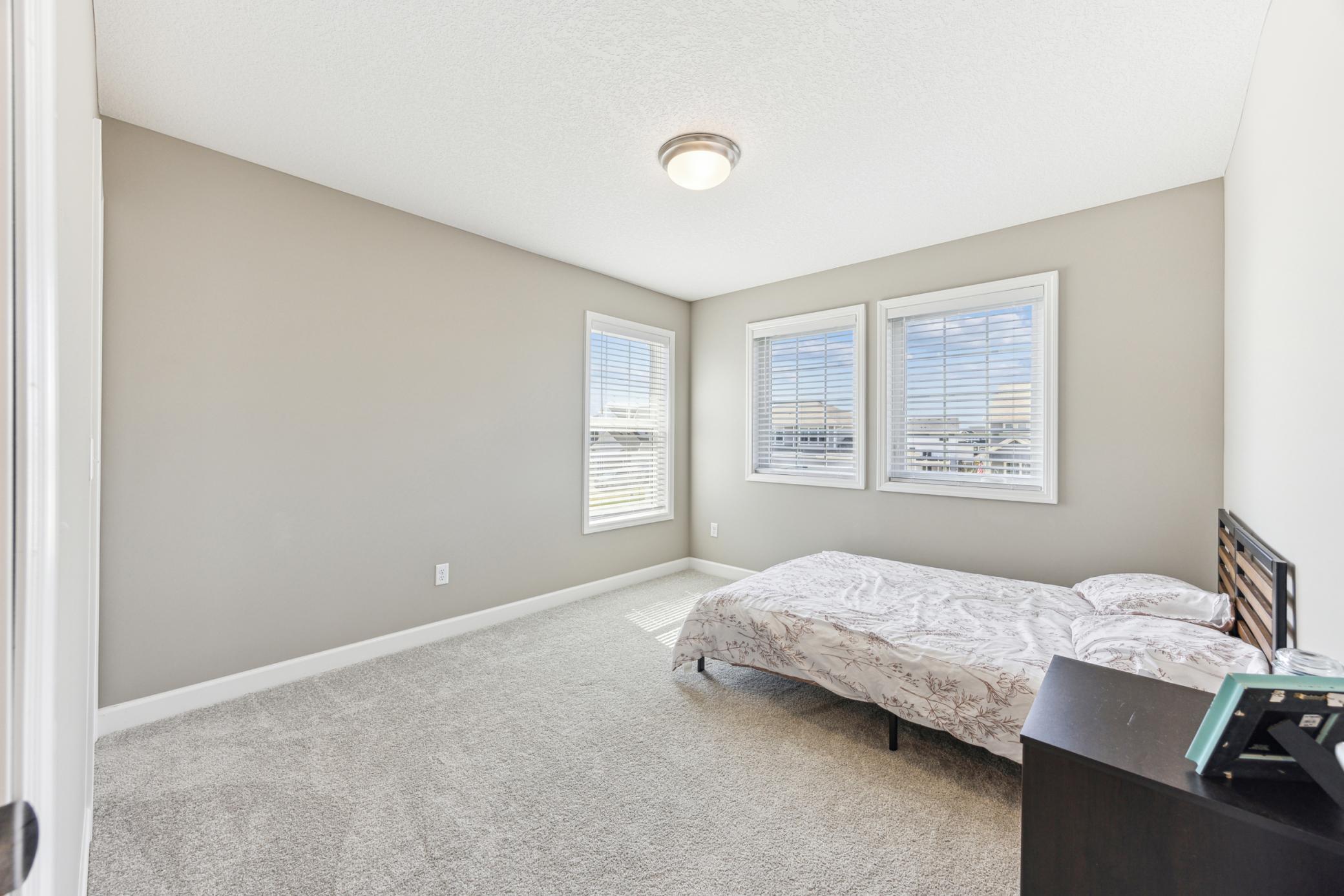 Bedroom with a bed, gray carpet, and three windows with white blinds.