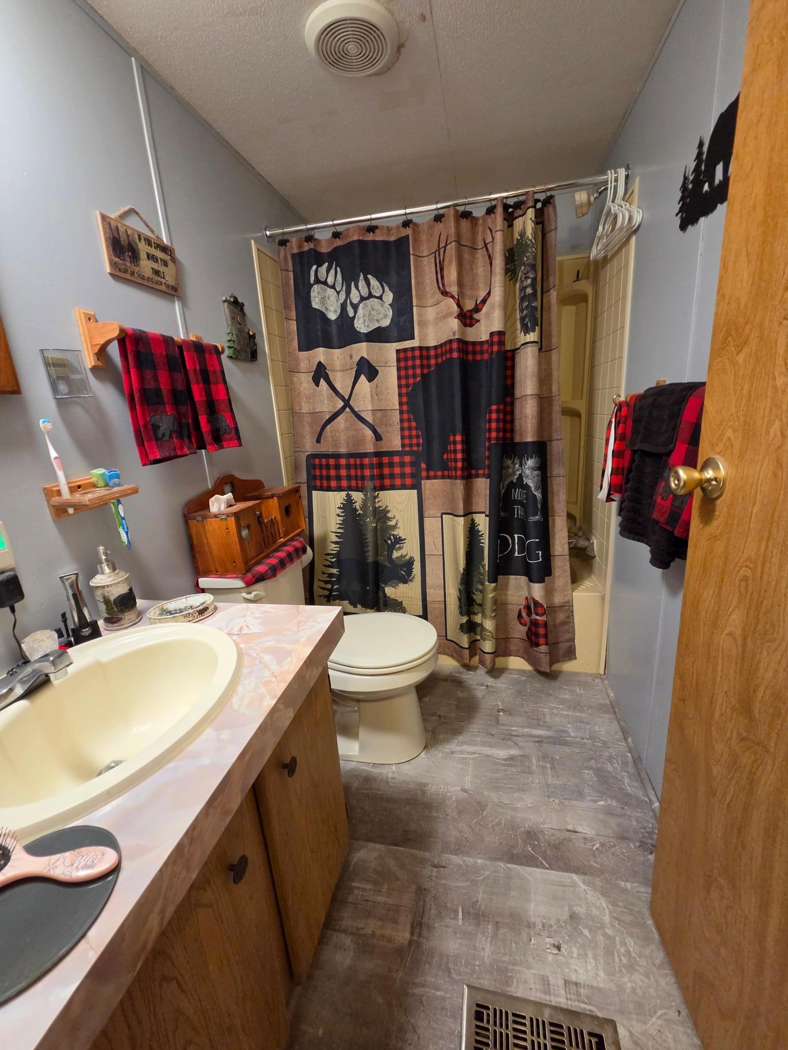 Bathroom with a wood vanity, gray tile floor, and woodland-patterned shower curtain.