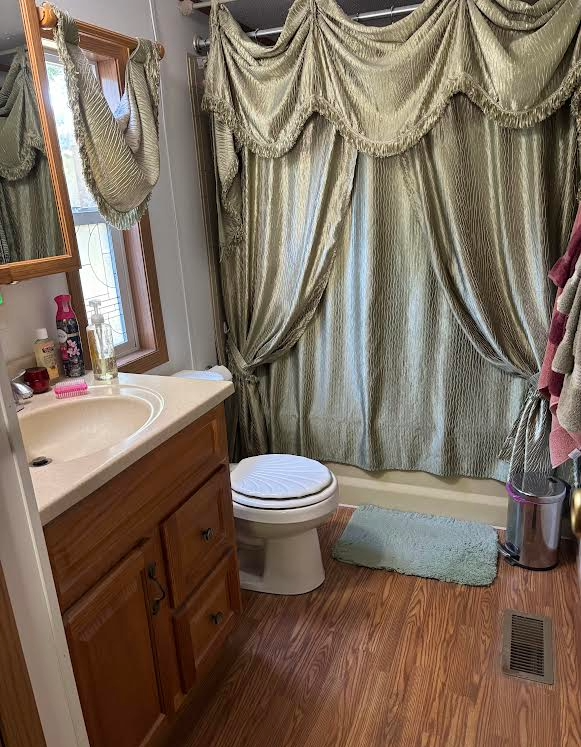 Bathroom with a wood vanity, toilet, and bathtub concealed by green curtains.