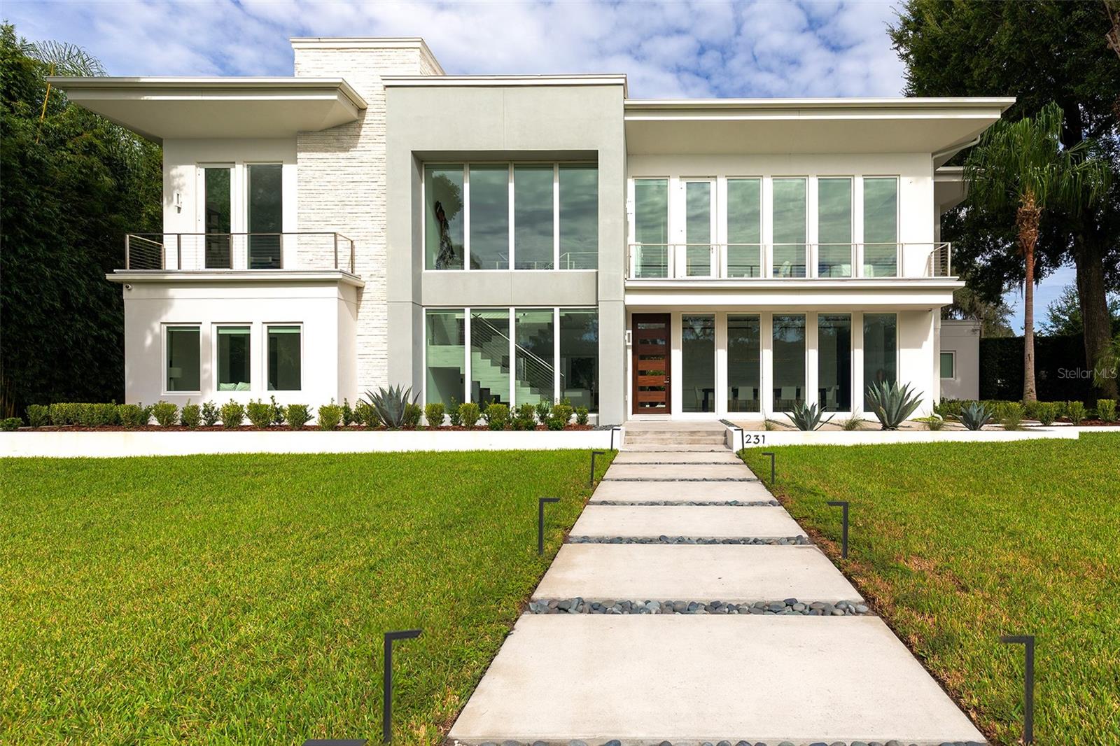 Modern white two-story home with glass balconies and a walkway across the lawn.