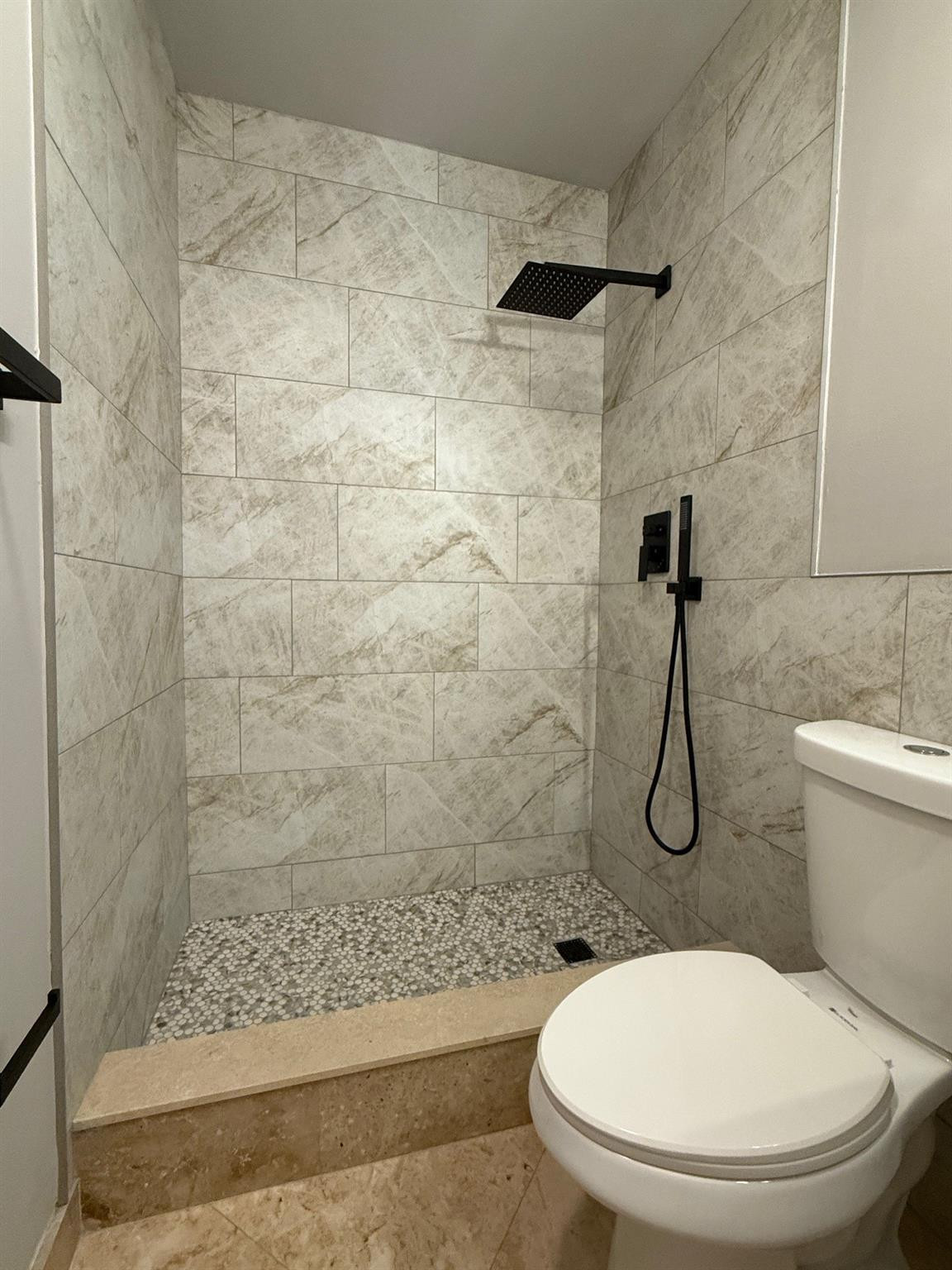 Bathroom with a pebble-floor walk-in shower, gray stone-look tile, and matte black fixtures.
