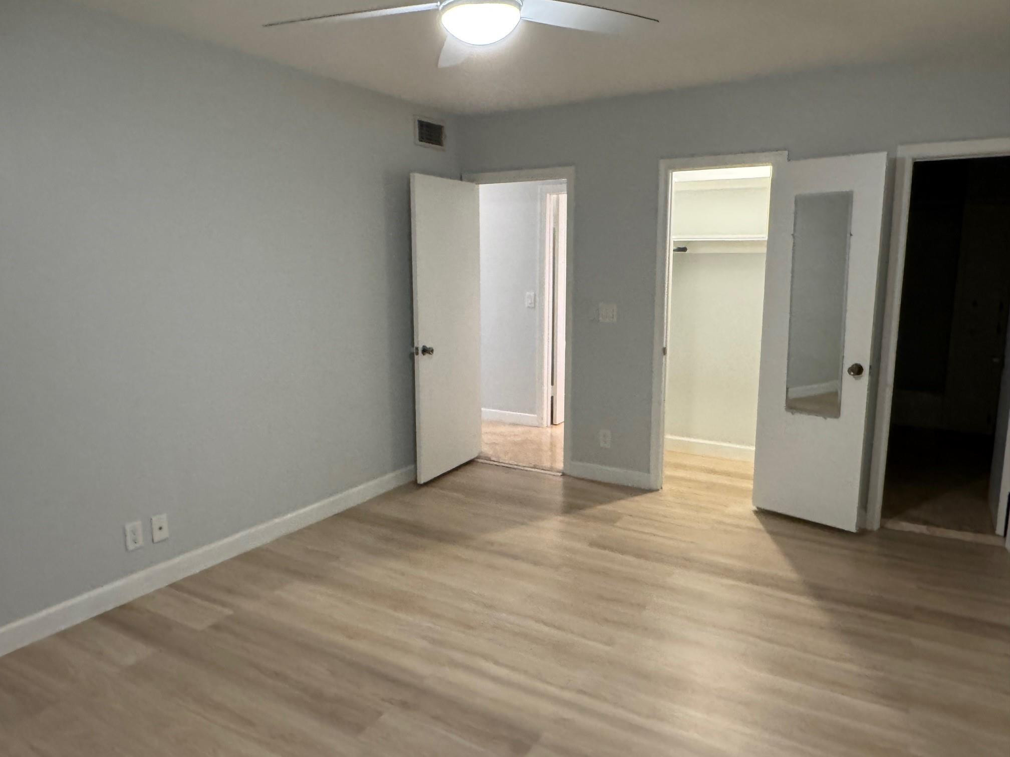 Empty bedroom with light wood floors, gray walls, and open closet doors.
