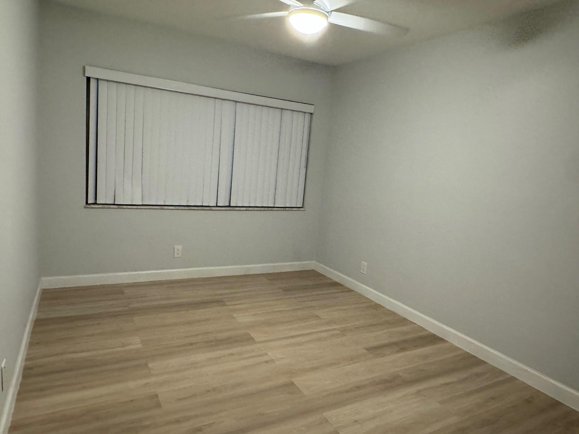 Empty room with light wood-look flooring, closed vertical blinds, and a ceiling fan.
