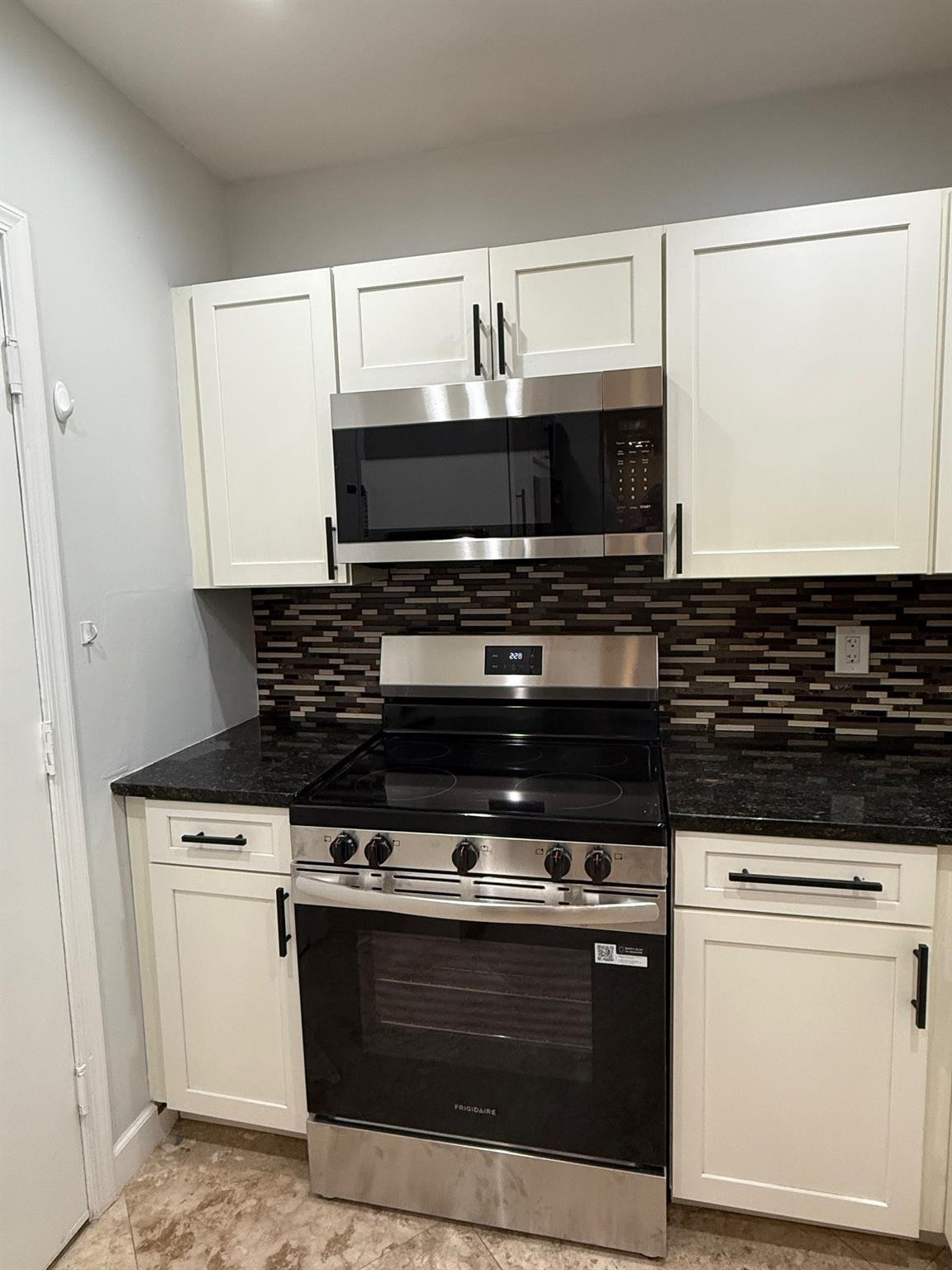 Kitchen with white cabinets, dark countertops, mosaic backsplash, and stainless steel range and microwave.