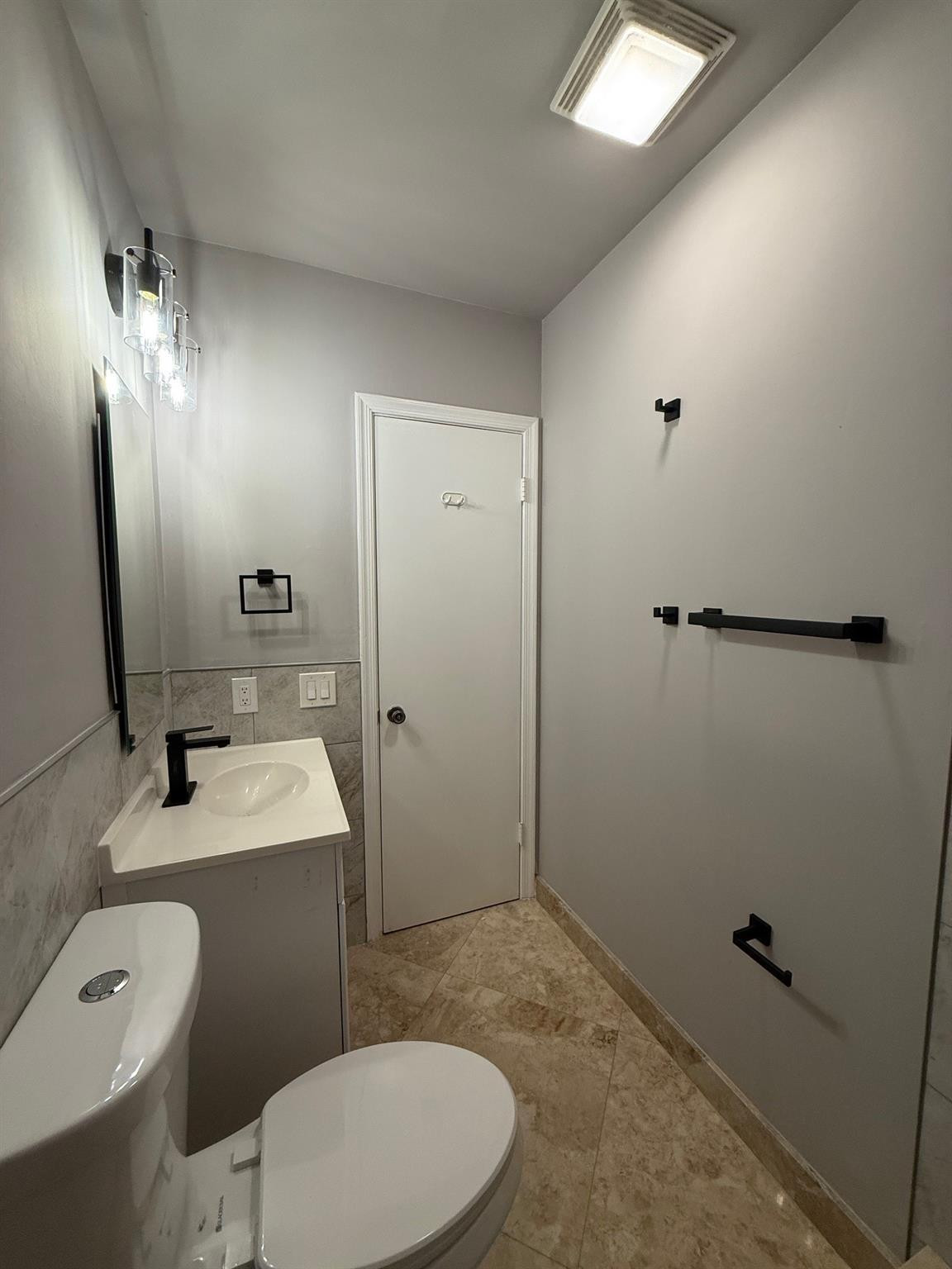 Updated bathroom with a white vanity, toilet, beige tile, and black fixtures.