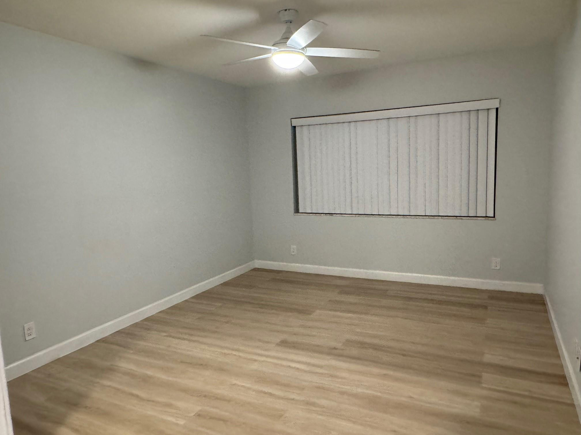 Empty room with wood-look flooring, vertical blinds, and a ceiling fan with light.