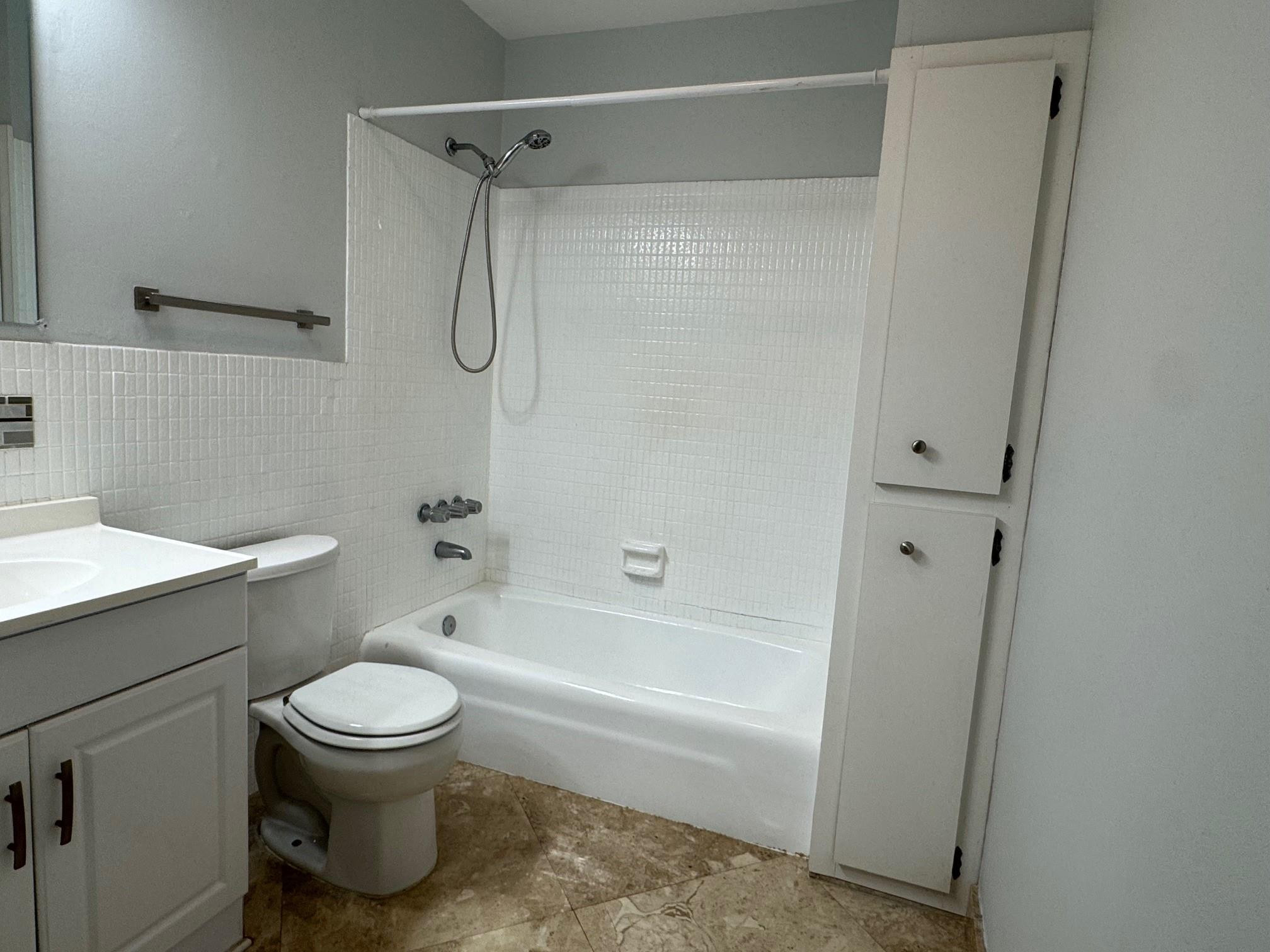 Bathroom with a tiled tub and shower, toilet, vanity, and tall built-in cabinet.