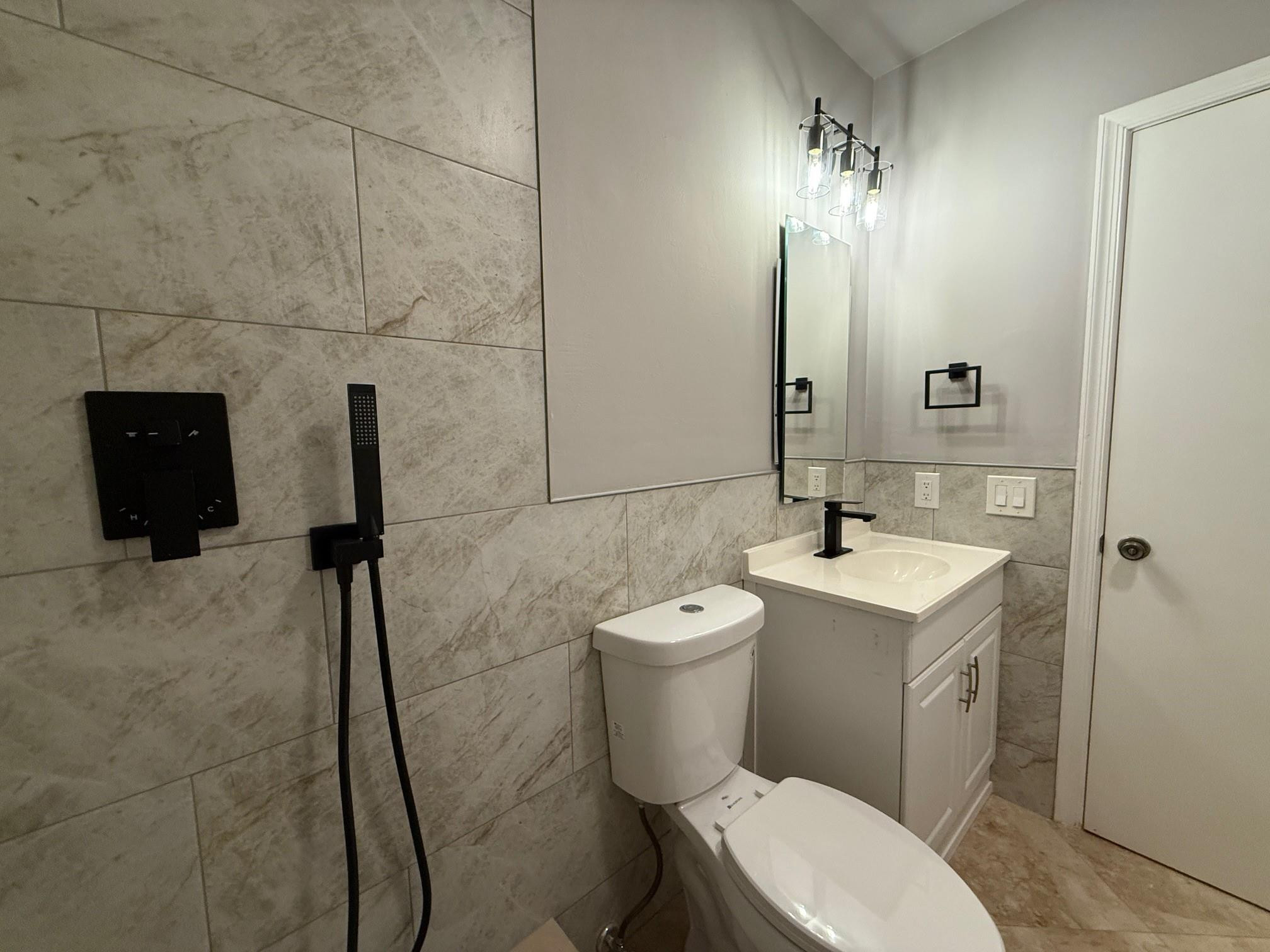 Bathroom with gray stone-look tile, black shower fixtures, and a white vanity.