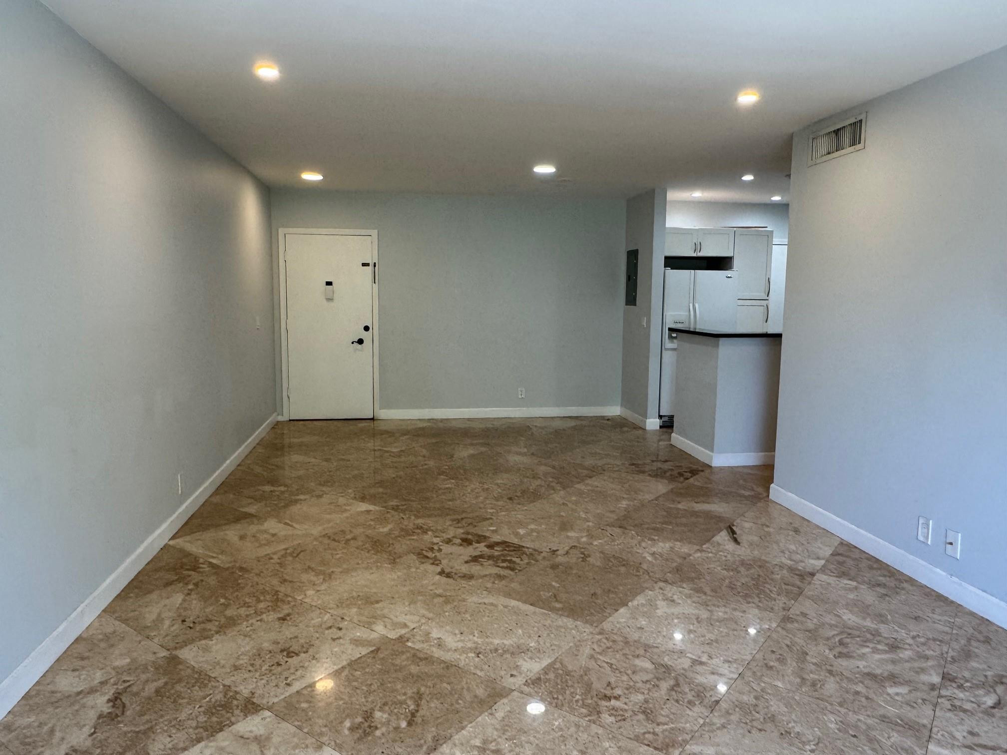 Vacant living area with glossy stone tile floors and a compact kitchen at the back.